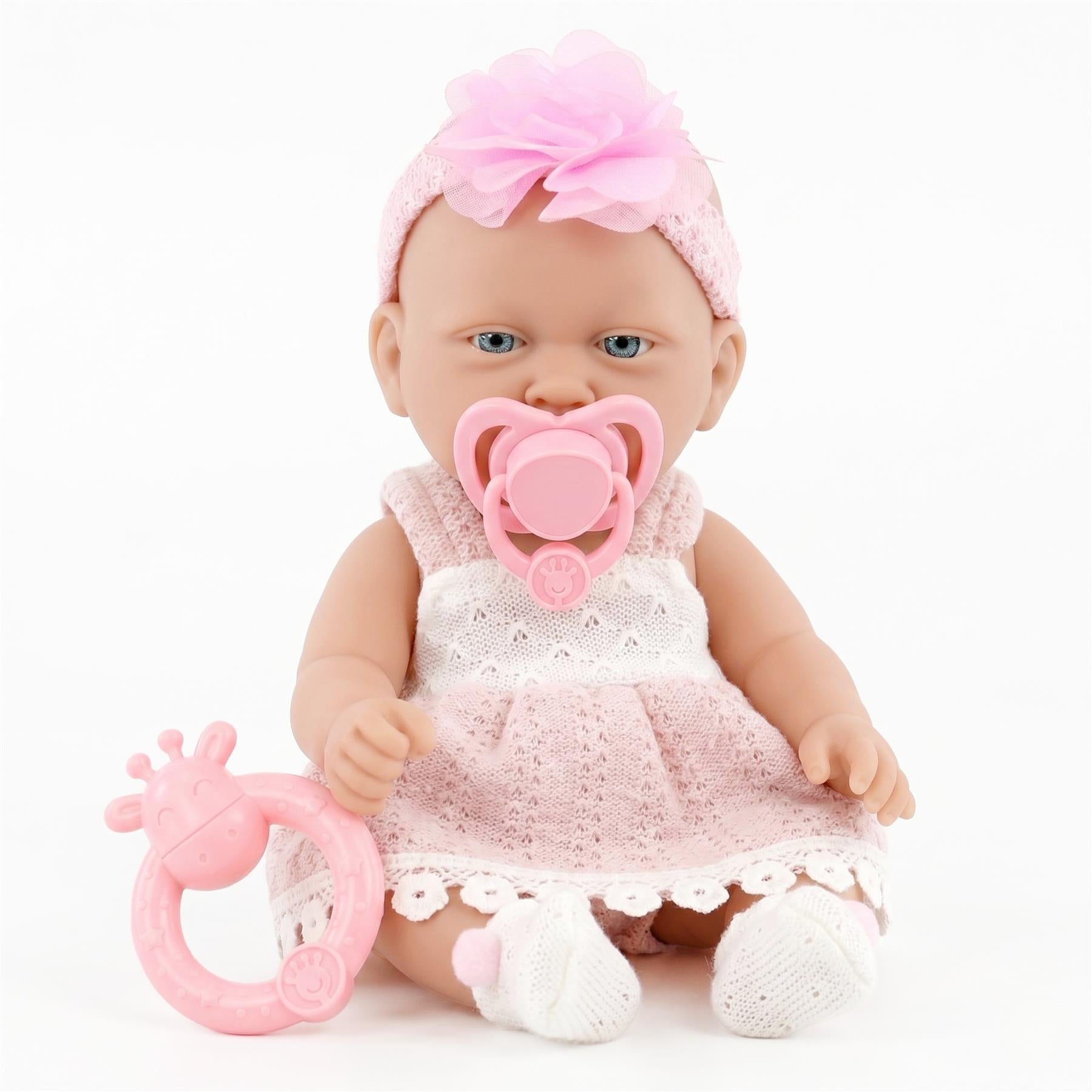 Pink baby doll dressed in a skirt, resting next to a matching pink rattle toy.