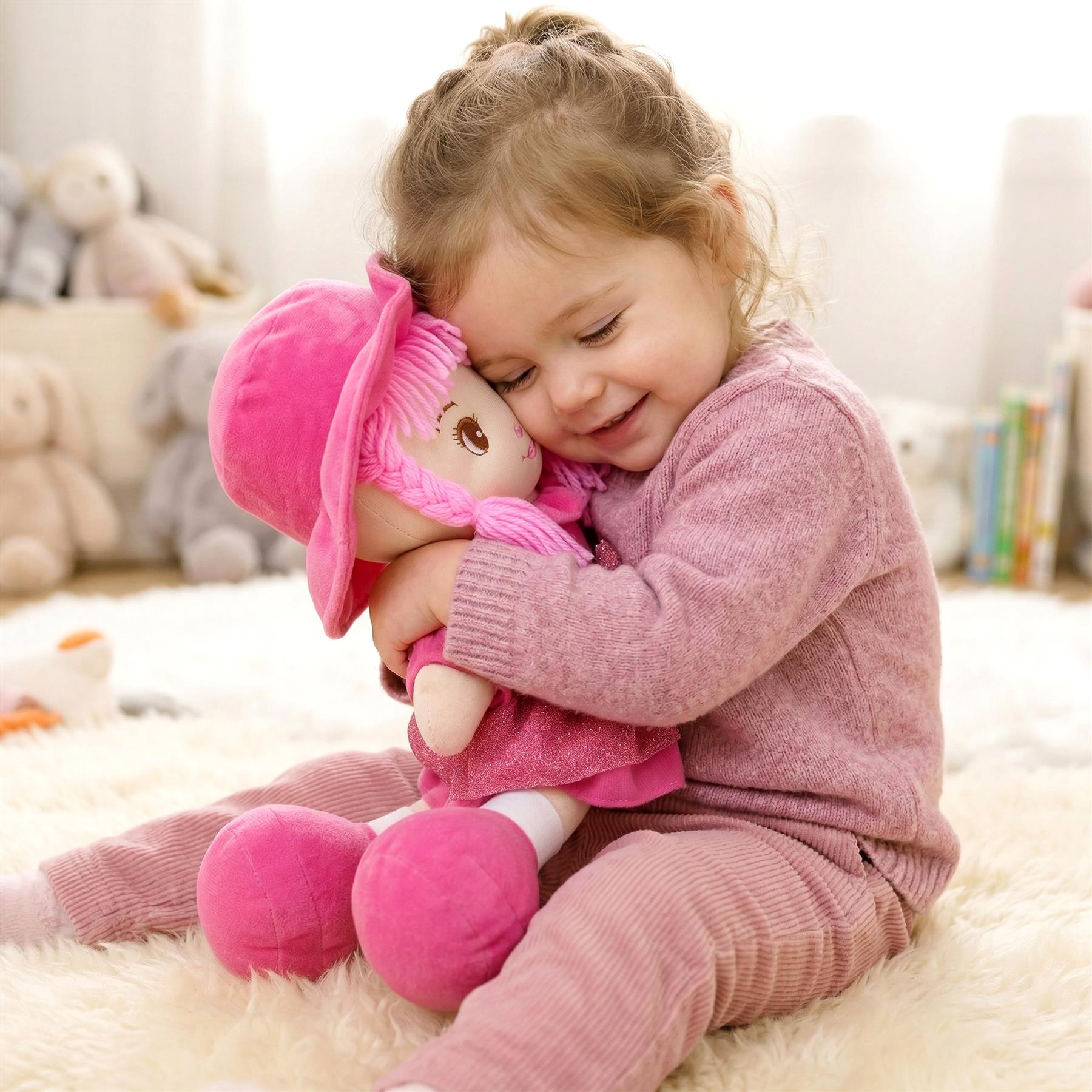 A young girl holds a plush doll with a pink wig and matching outfit while seated on a white rug.