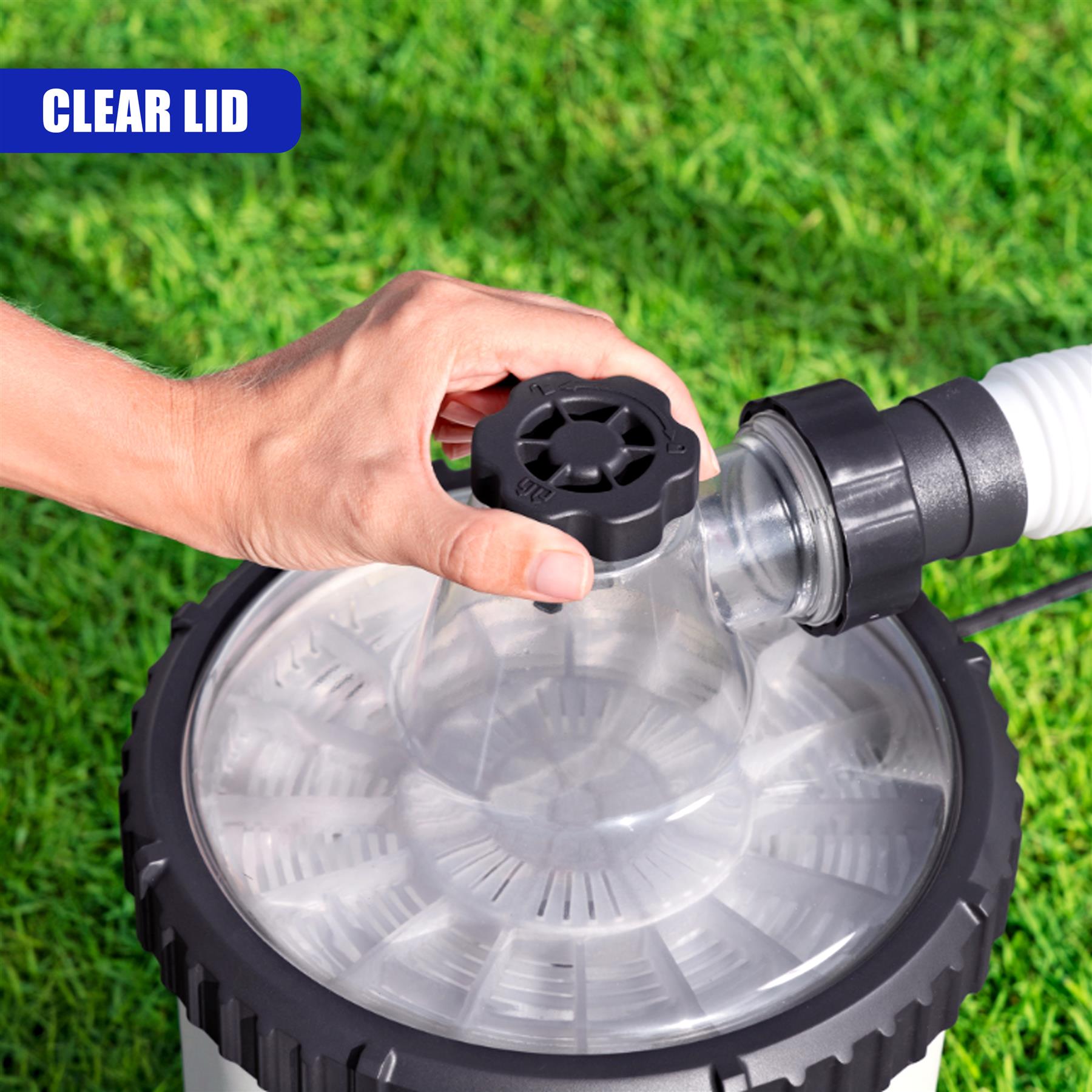 A hand connects a black fitting to a large, round, clear pool filter lid resting on green grass.
