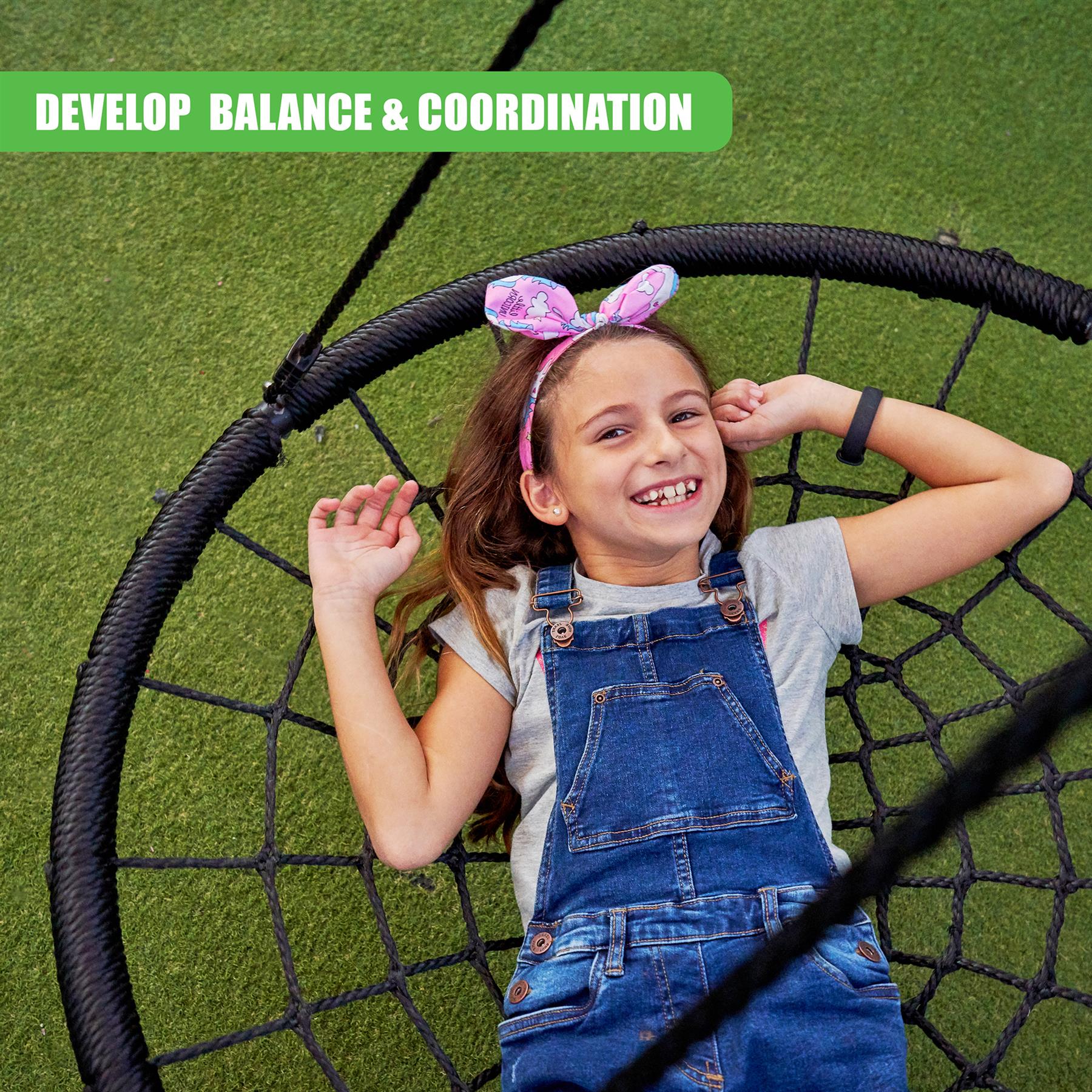 A smiling girl in denim overalls sits on a large black suspended nest swing.