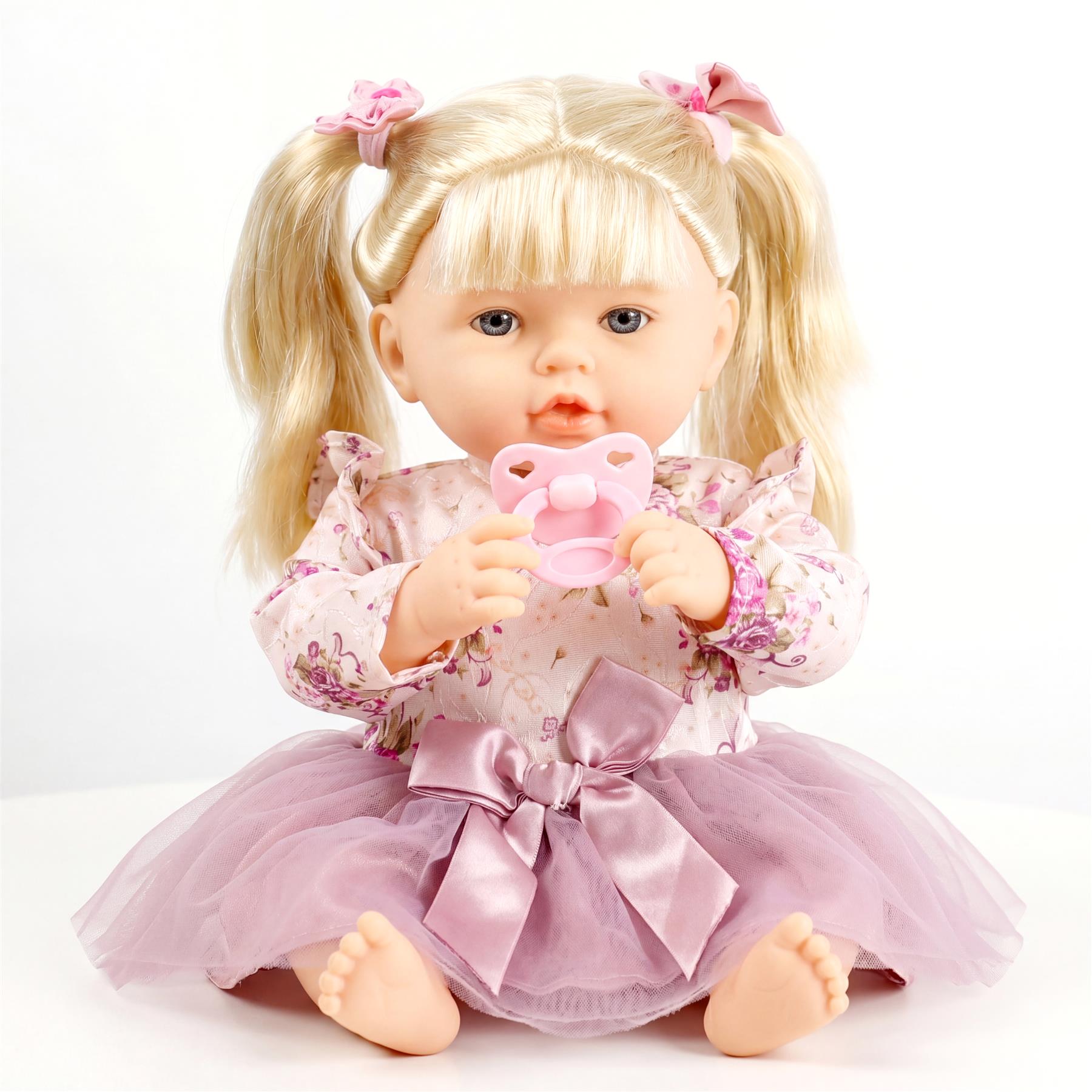 Blonde doll with pigtails, wearing patterned clothes, holding a pink pacifier prop.