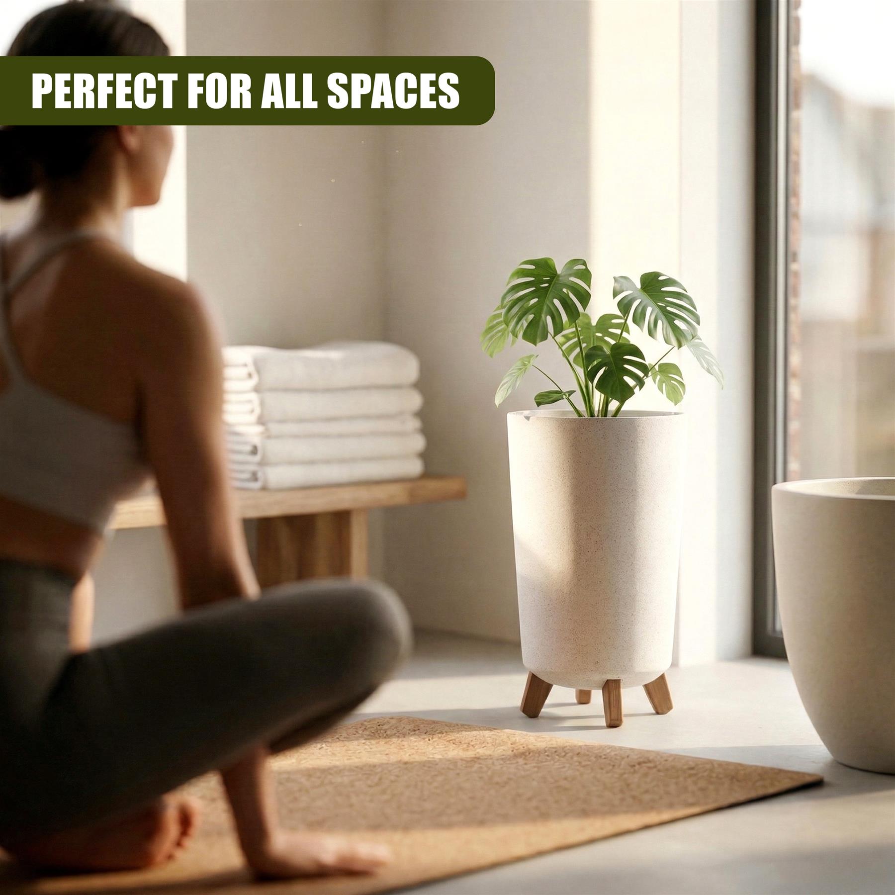 A tall, white container pot with wooden legs holds a green houseplant indoors near folded white towels.