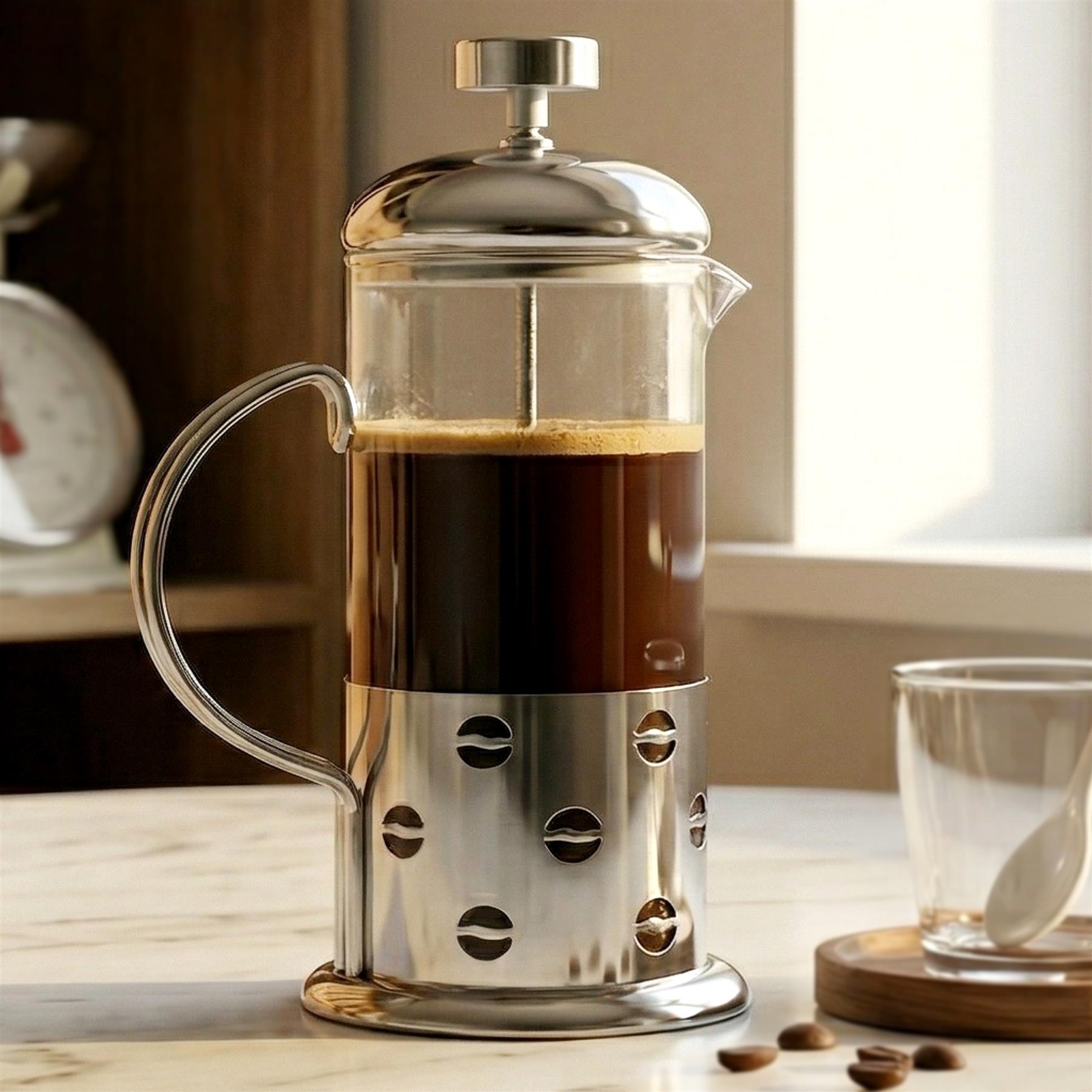 Silver metal cafetière filled with brewed coffee sits on a light counter next to a cup.
