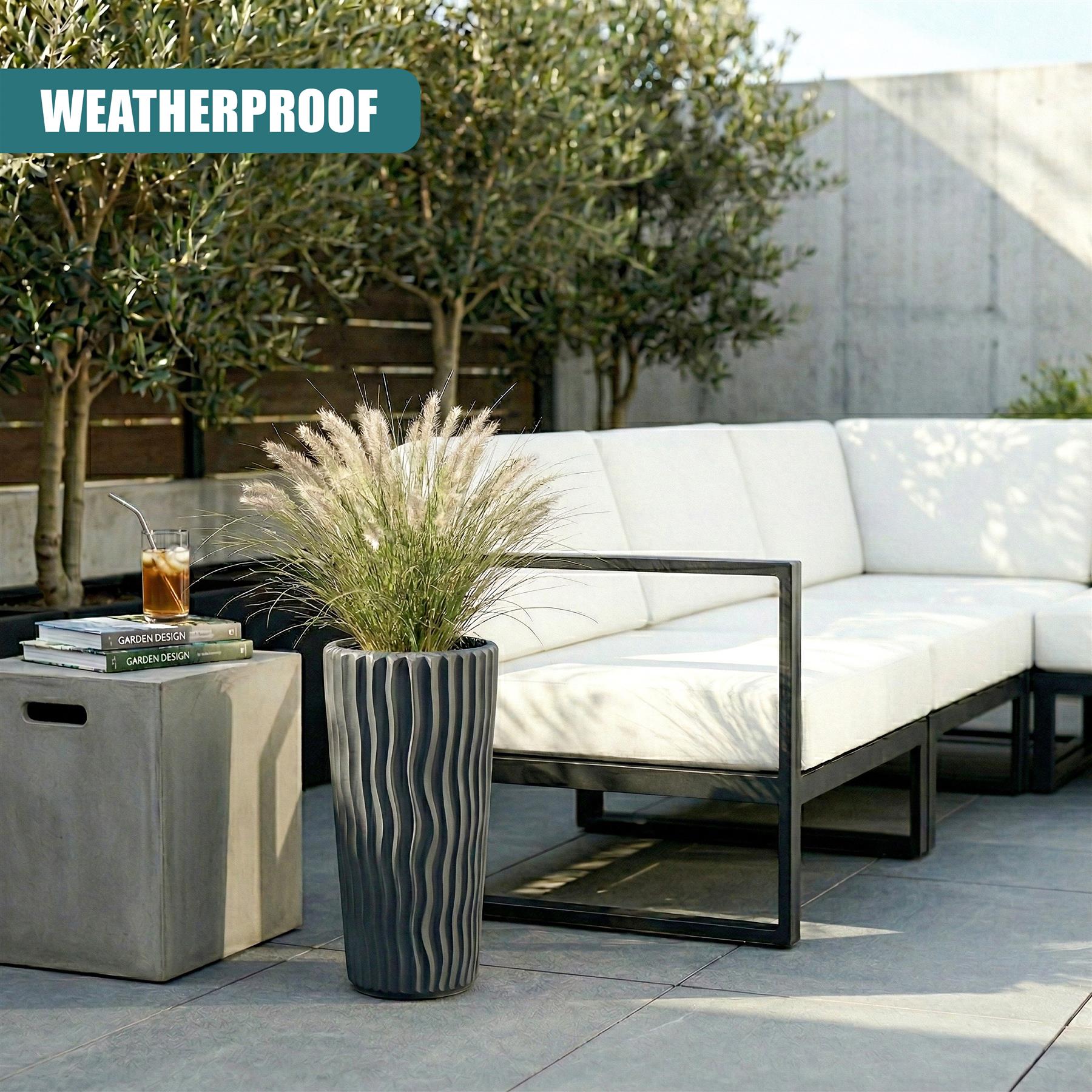 Tall, striped anthracite flower pot containing light-colored ornamental grasses on an outdoor patio.