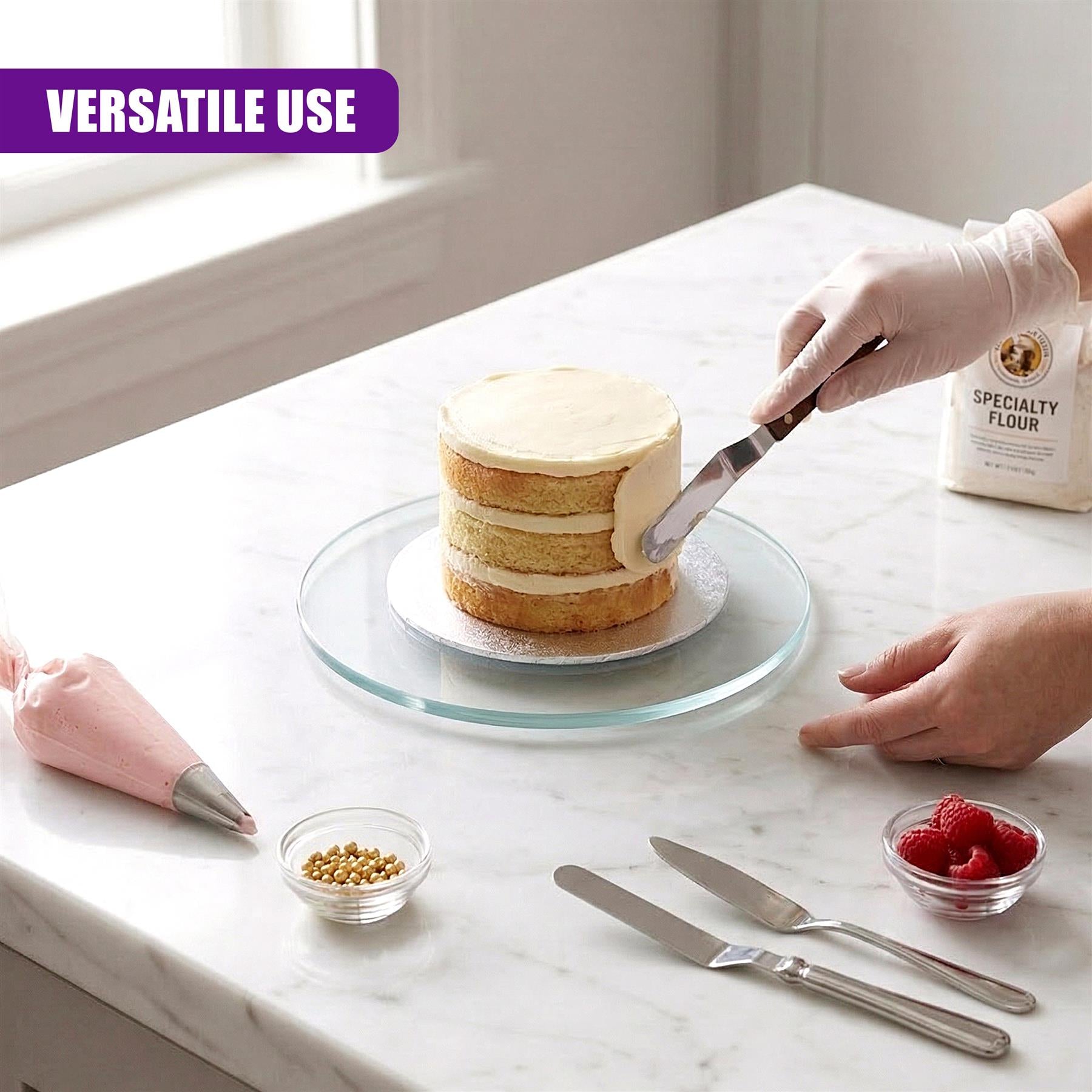 On a marble counter, a cake rests on a round glass turntable near baking supplies.
