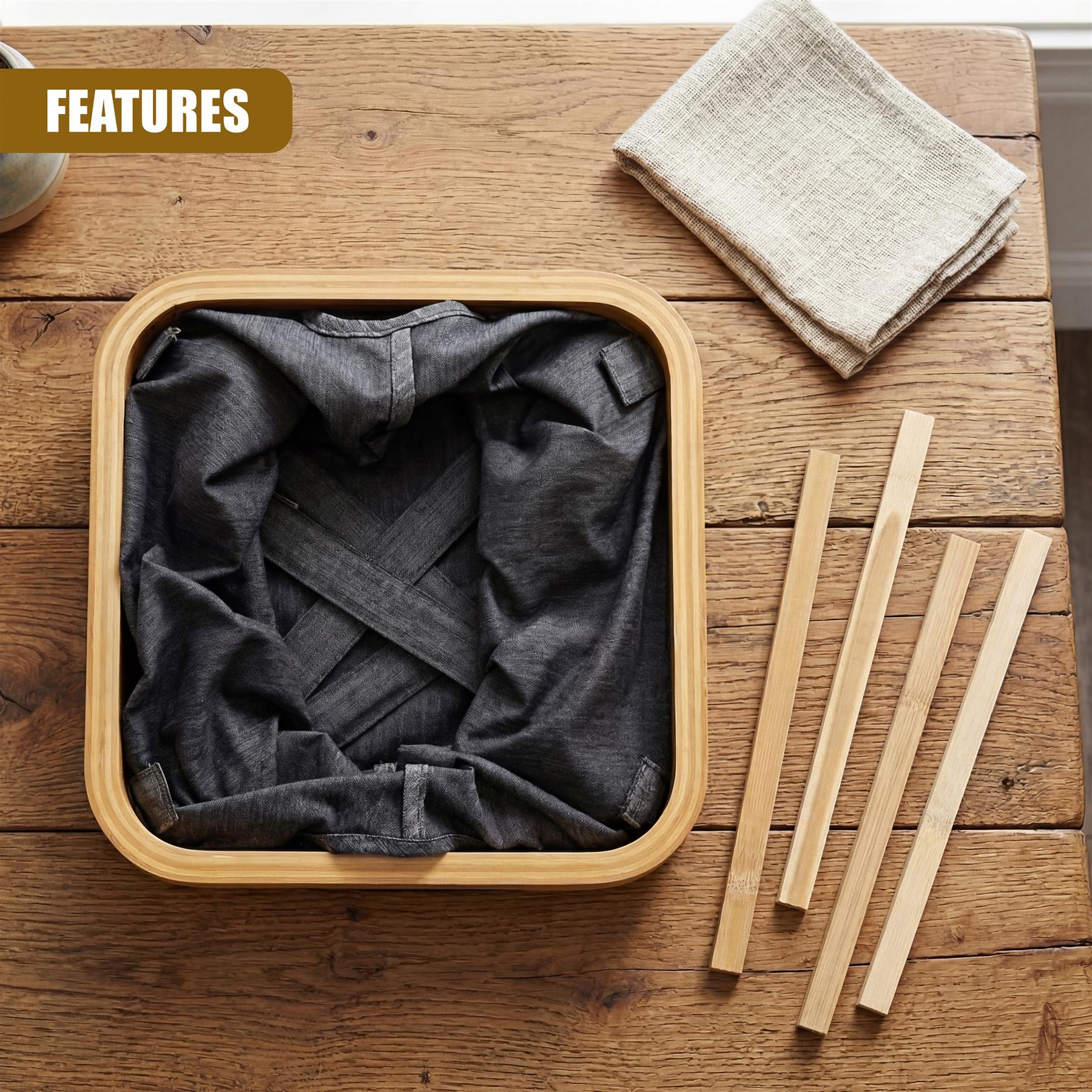 Dark gray hamper in a wooden tray next to folded natural linen cloth and three smooth wooden sticks.