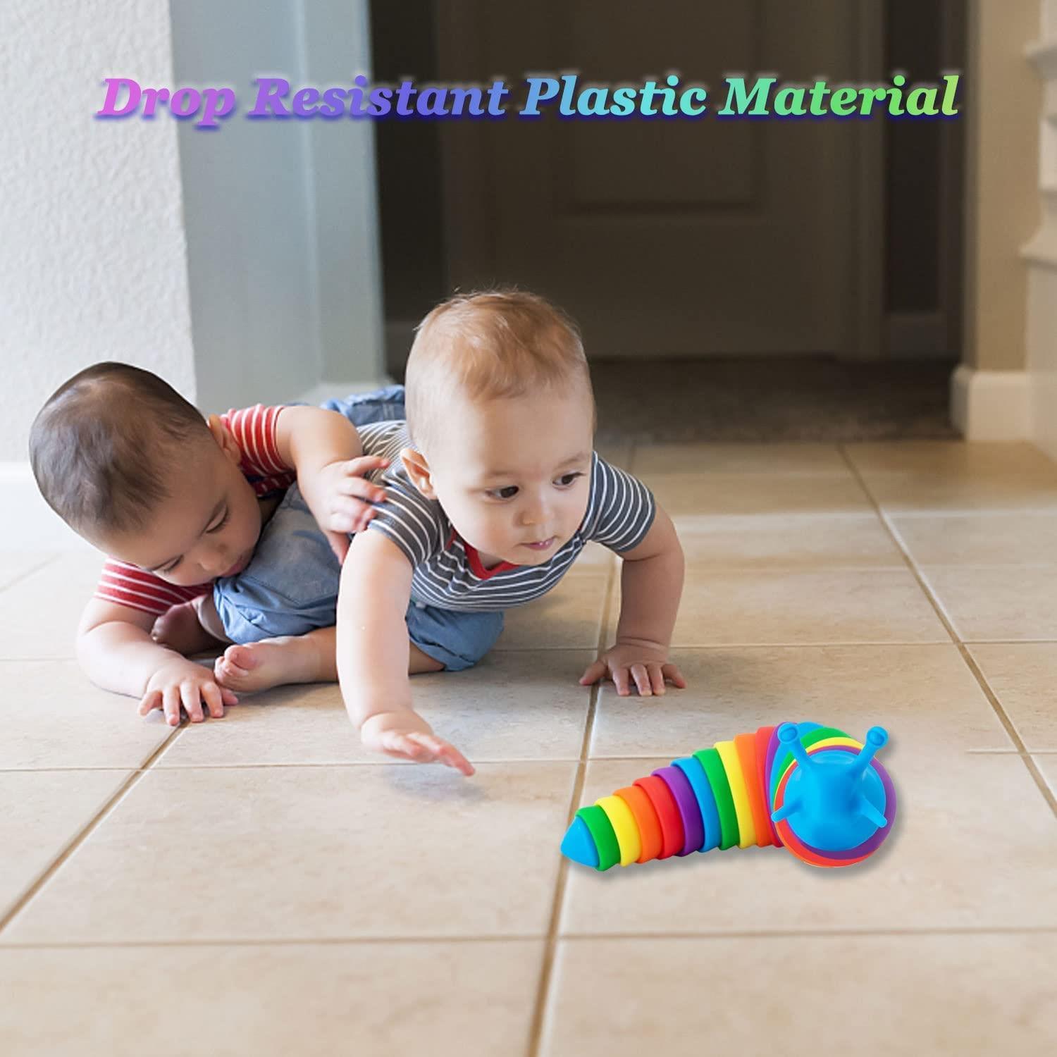 Two babies crawl on a tile floor next to a colorful, segmented fidget slug toy.
