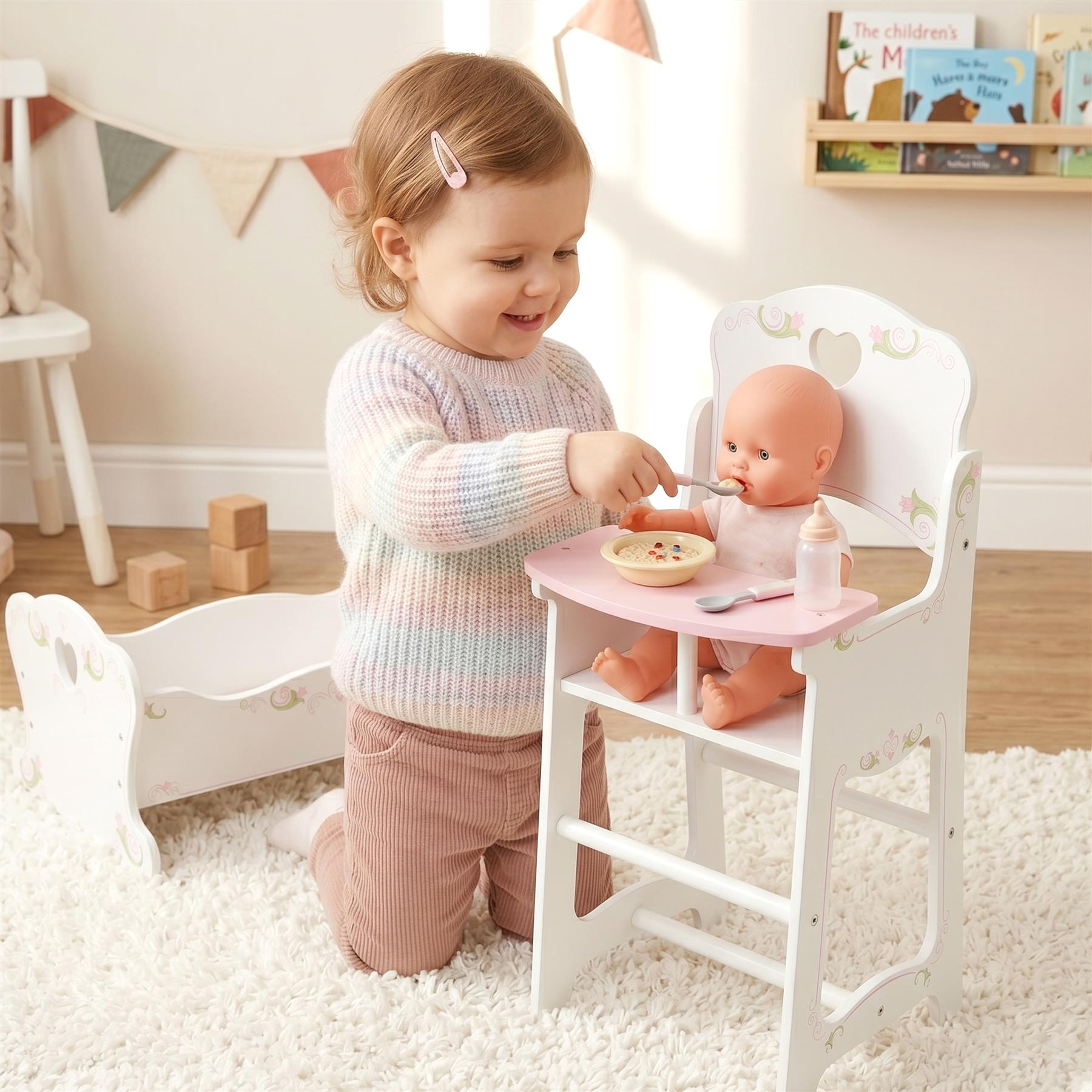 Little girl interacts with doll at play setting featuring wooden high chair and cradle.