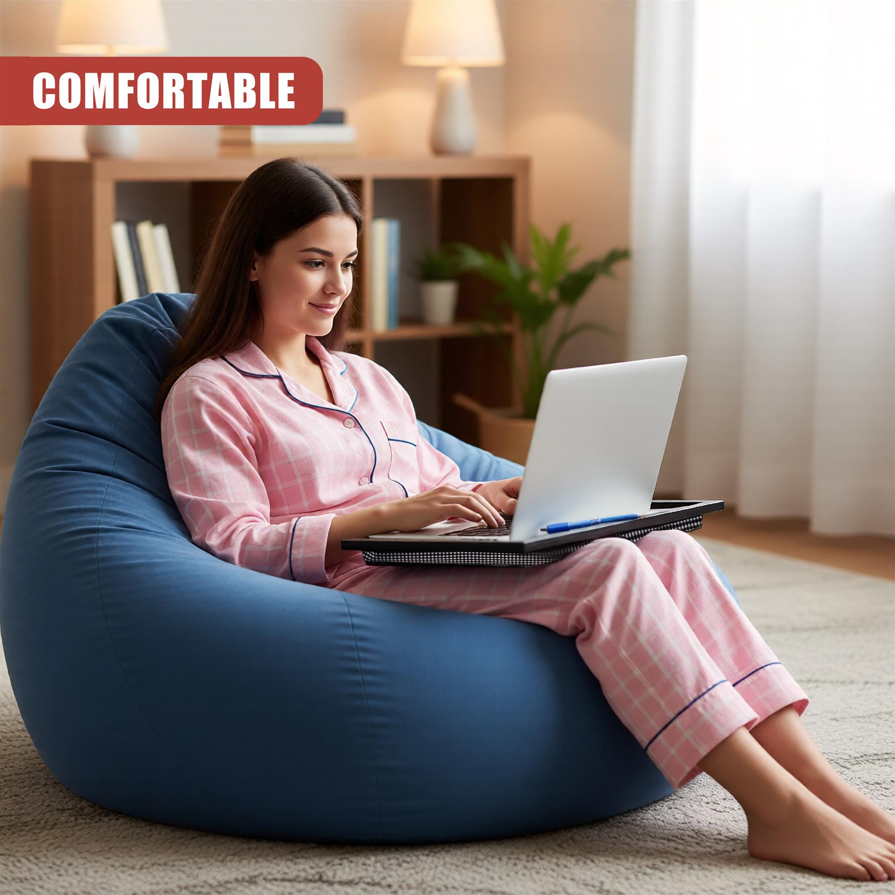 Woman sits on blue cushion, using a laptop and lap tray at home.