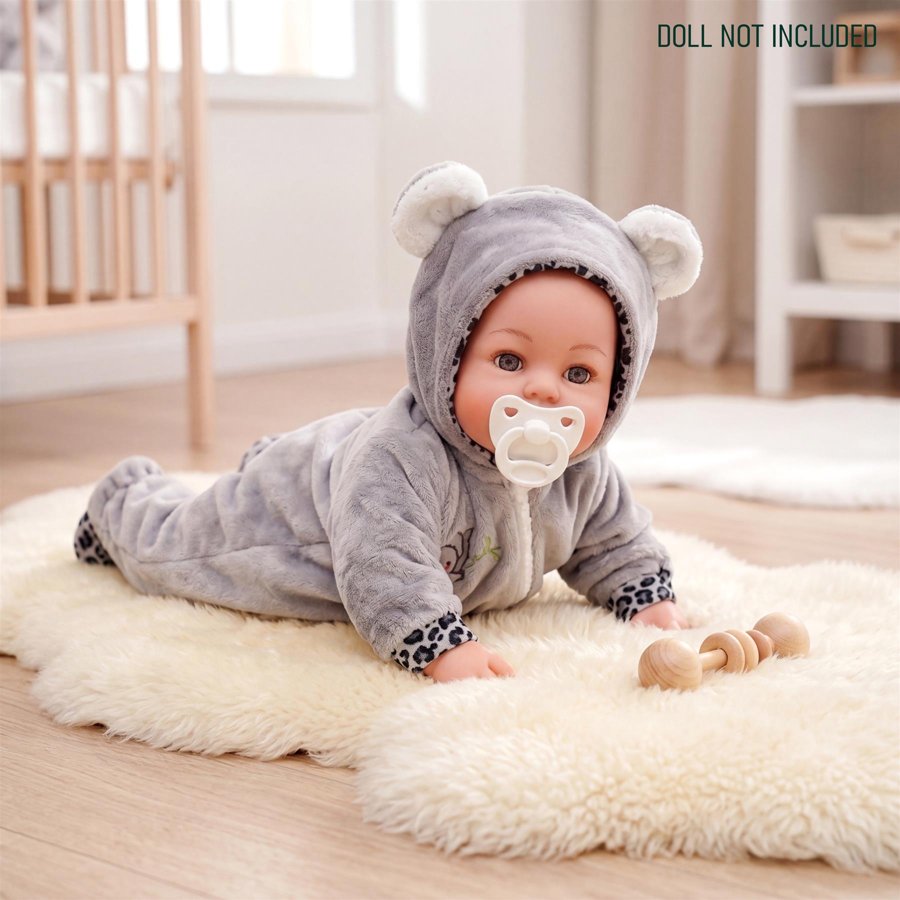 Doll wearing a gray hooded sleeper, lying on a white rug with associated wooden teethers.