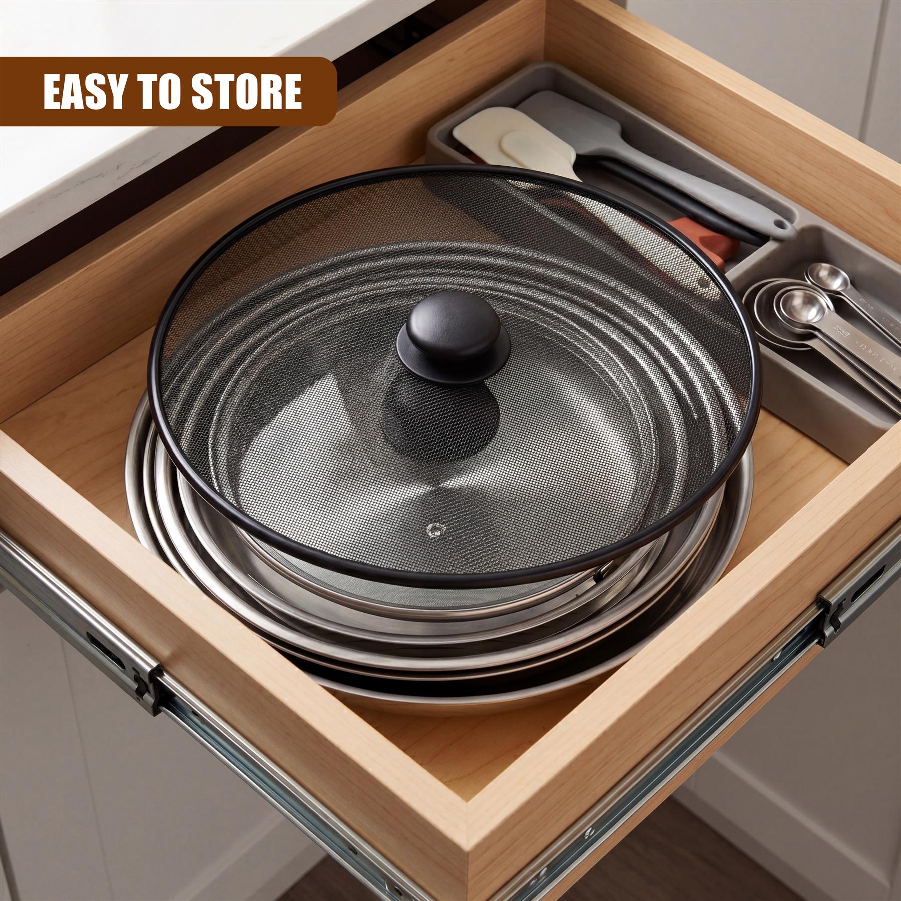 A black mesh splatter screen rests on a stack of nested metal pots inside a kitchen drawer.