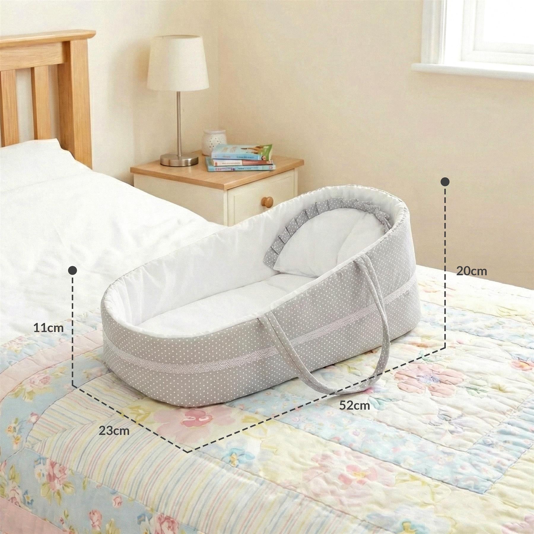 White crib with a grey blanket. It has a dotted pattern and handles on each side. There are two measurements indicated: height of the cot is 39cm, width is 64cm. It's placed in front of a bed. - The Magic Toy Shop