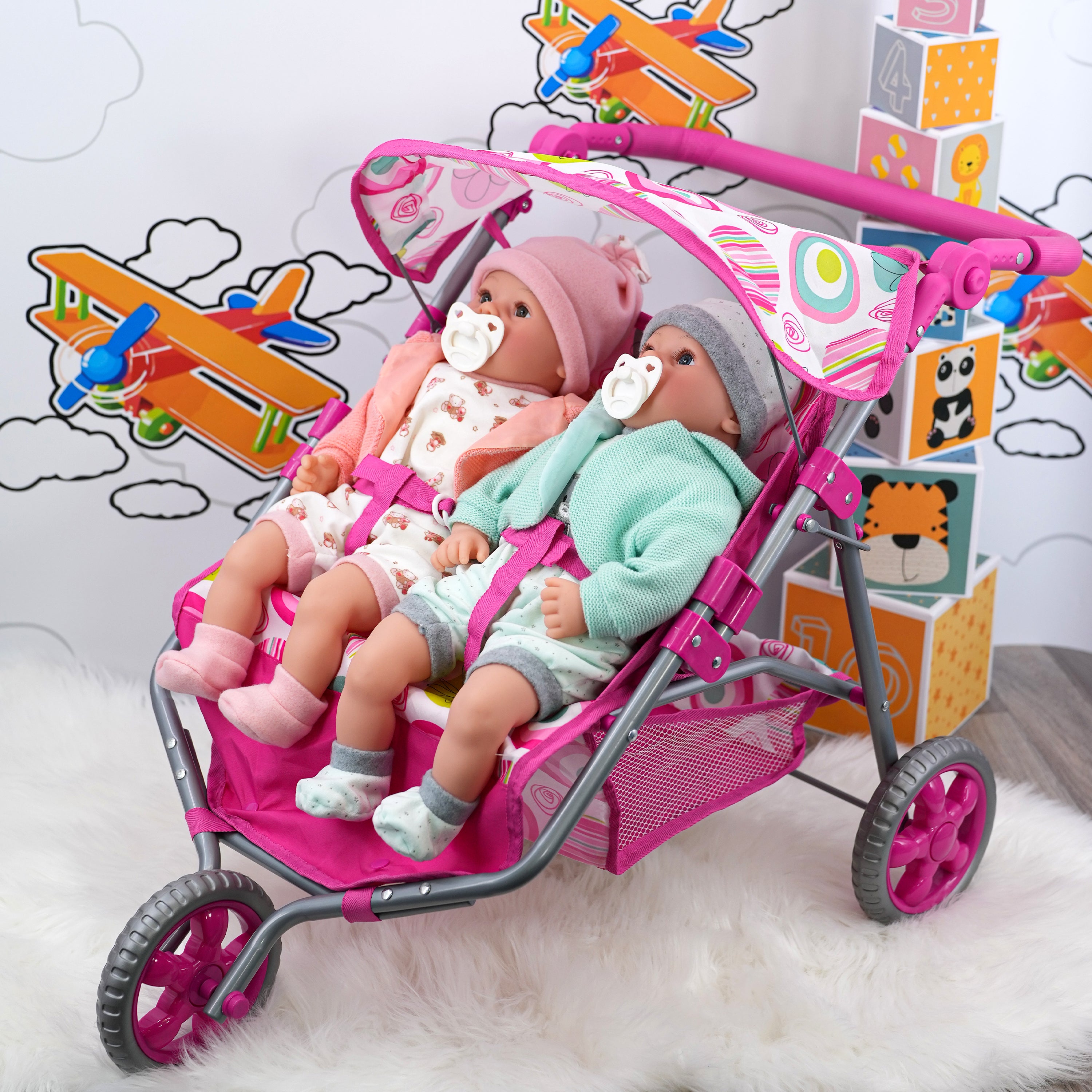 Pink three-wheeled doll stroller holding two seated dolls in contrasting pink and mint outfits.