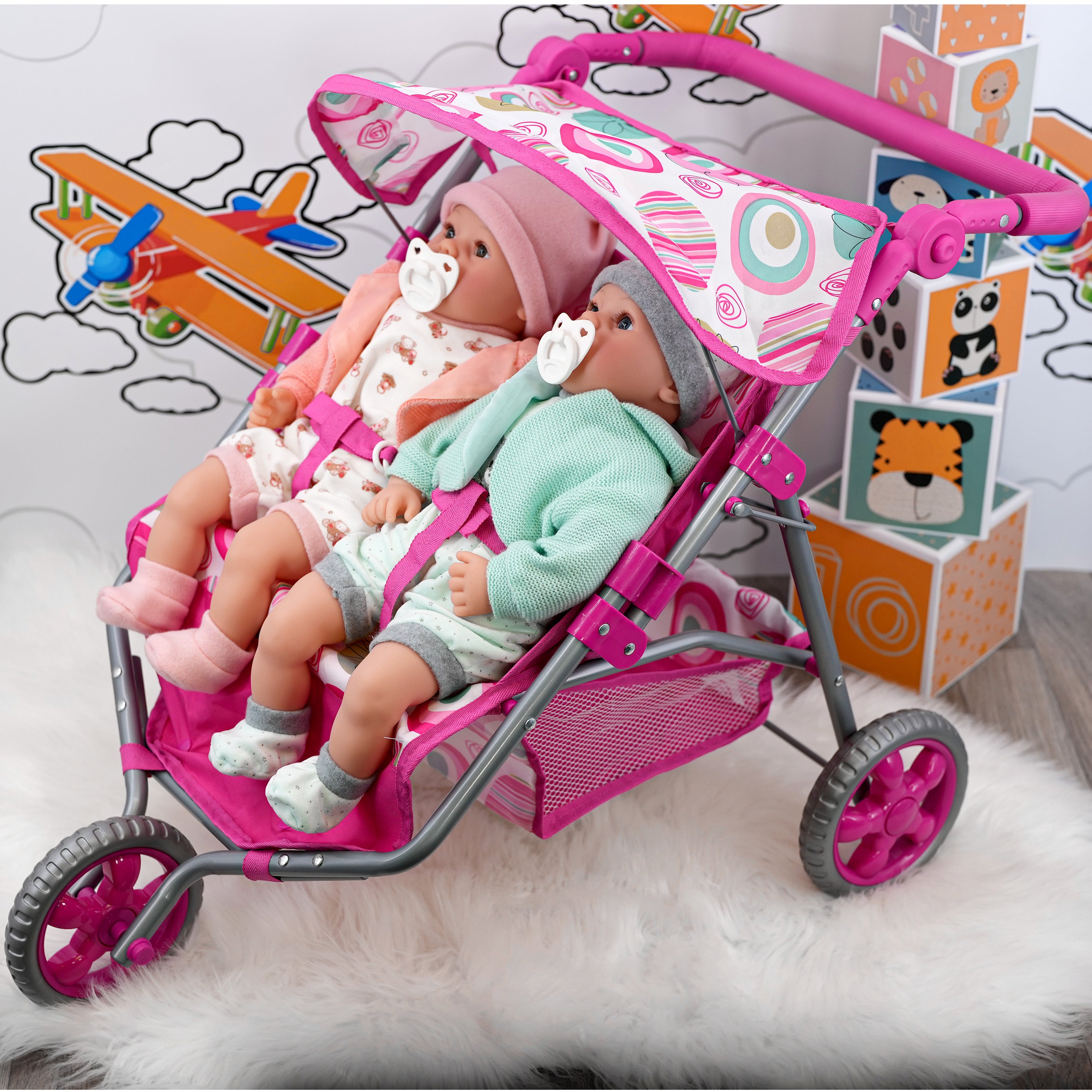 Pink twin doll pushchair with two dolls seated inside, placed on a fluffy rug.