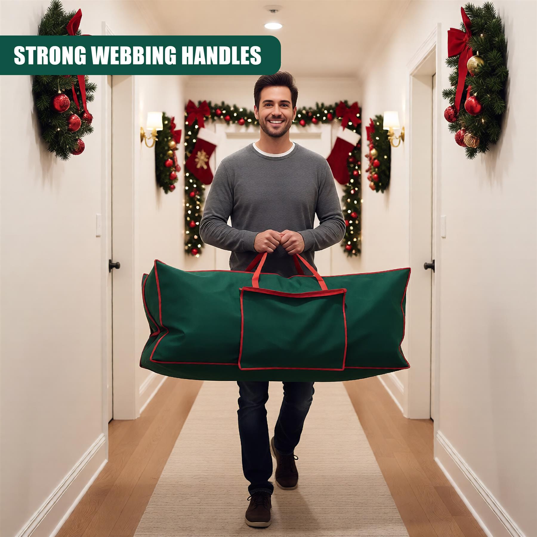 A man walks down a festive hallway, carrying a large green Christmas tree storage bag. The bag has a red trim and a handle on each end. The man is wearing a grey sweater and jeans, and the hallway is decorated with Christmas trees, wreaths, and stockings. - The Magic Toy Shop