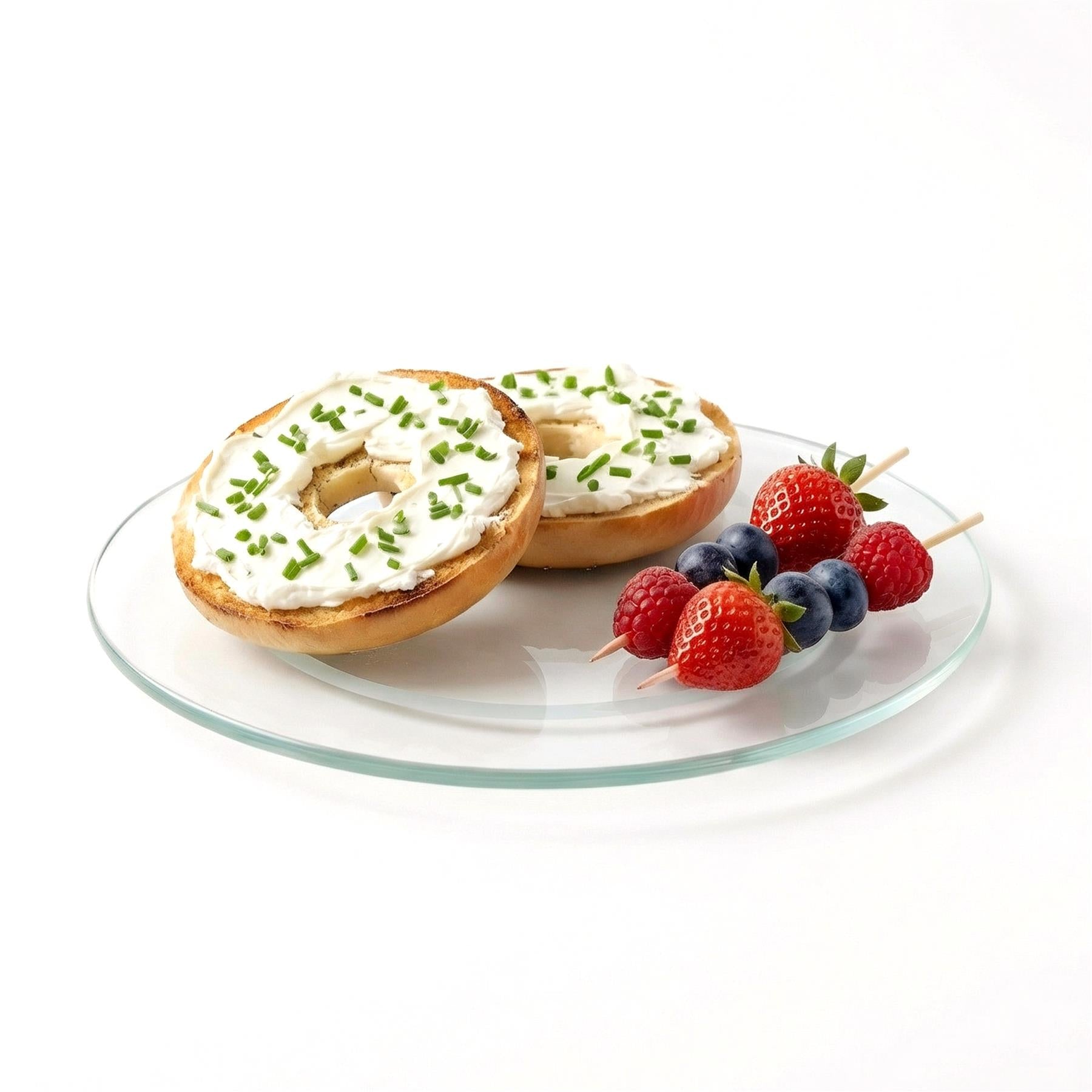 Bagels with cream cheese, fresh berries, and herbs are arranged on a clear glass serving platter.