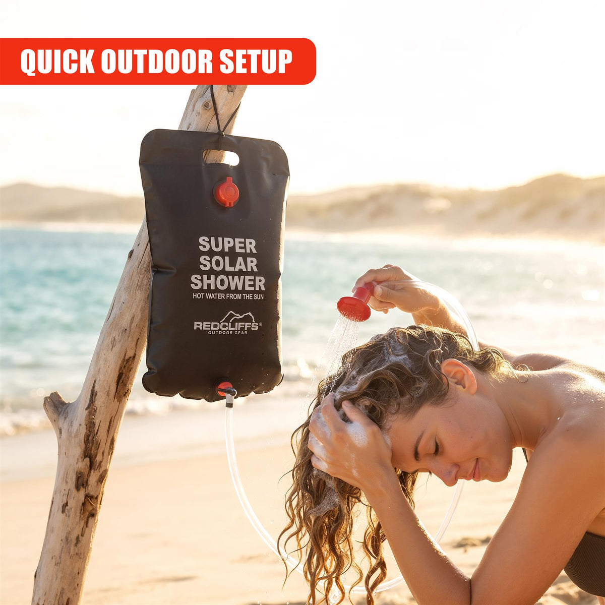 A woman uses a GEEZY Solar Shower Bag to enjoy a hot shower on a sandy beach