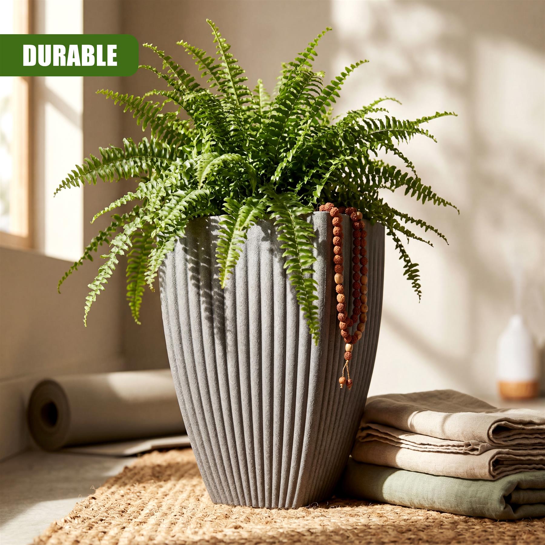 Gray, fluted planter with green fern foliage resting on a textured mat near folded linens.