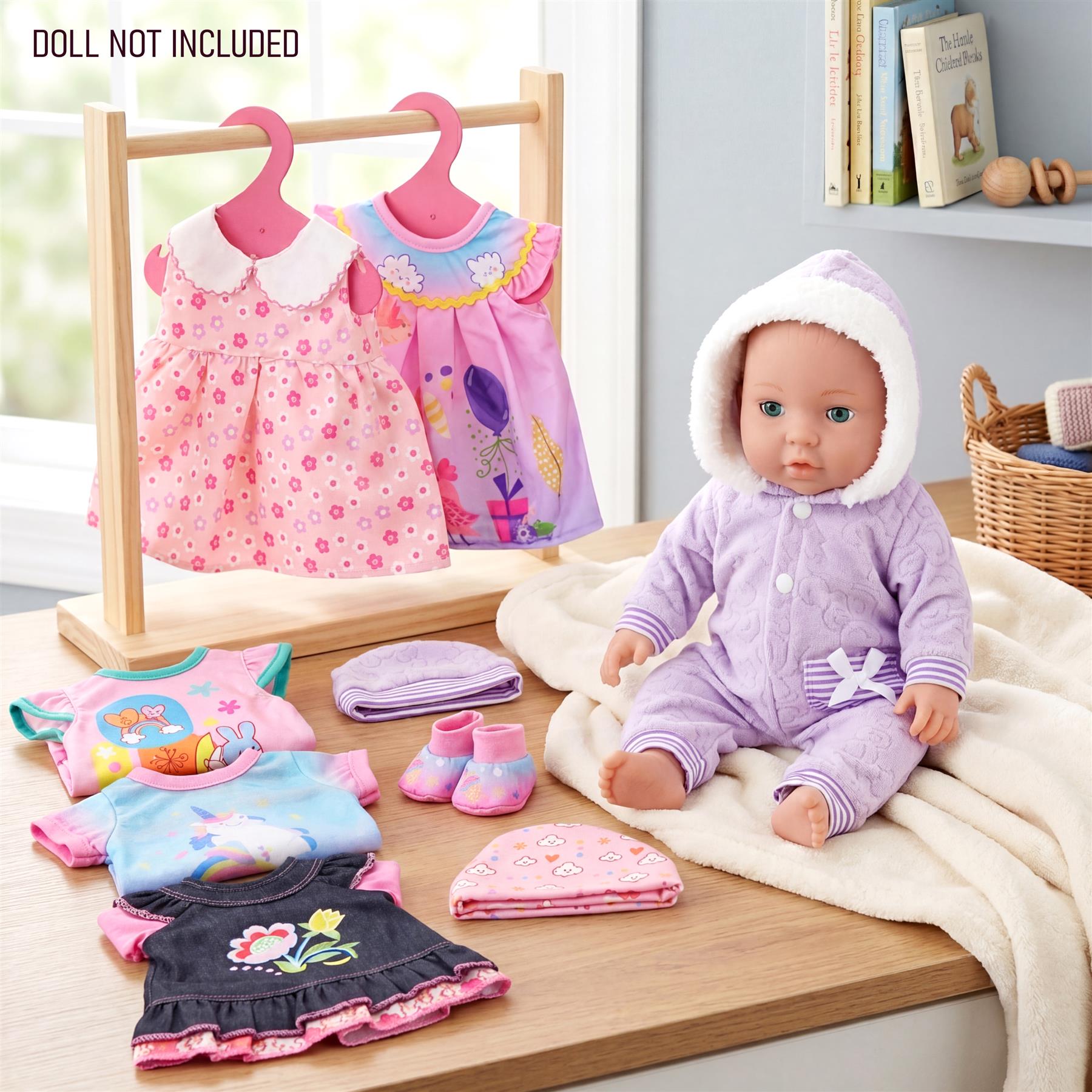 A baby doll sits on a cloth surrounded by various doll clothes, including floral dresses and matching accessories.
