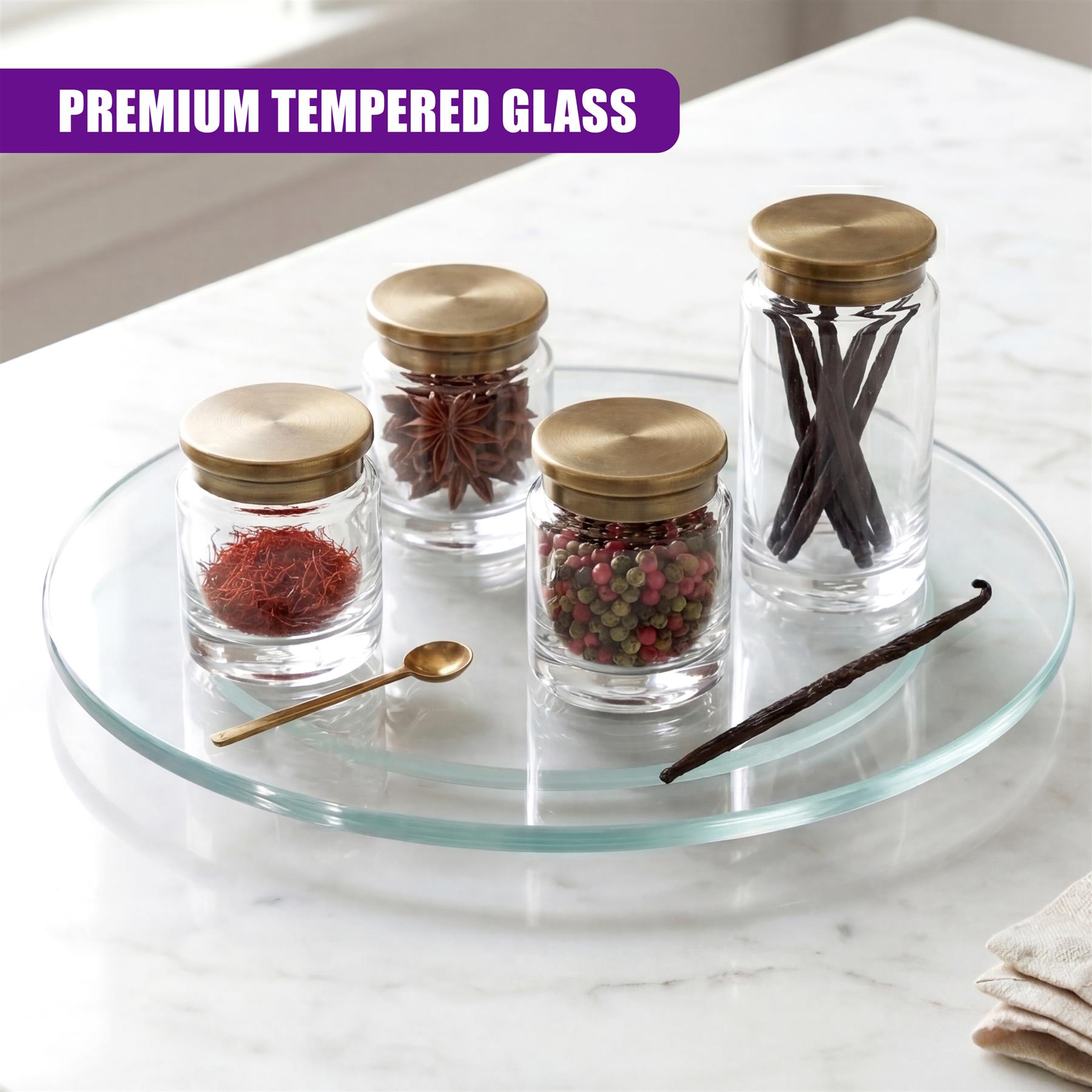 Clear glass turntable displaying three spice jars, cinnamon stick, and spoon on a white marble surface.