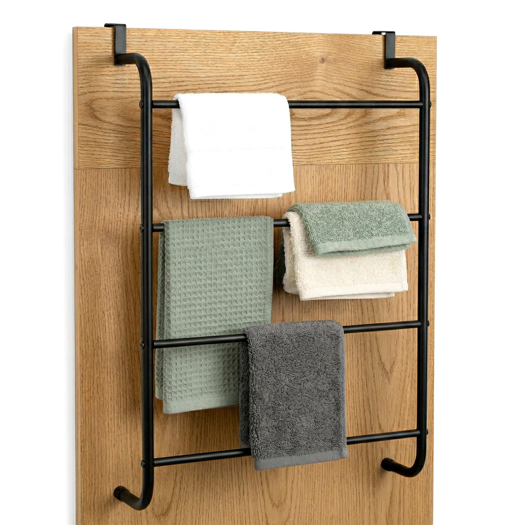 A black metal towel rail hangs on wood, displaying several folded white, green, and gray towels.