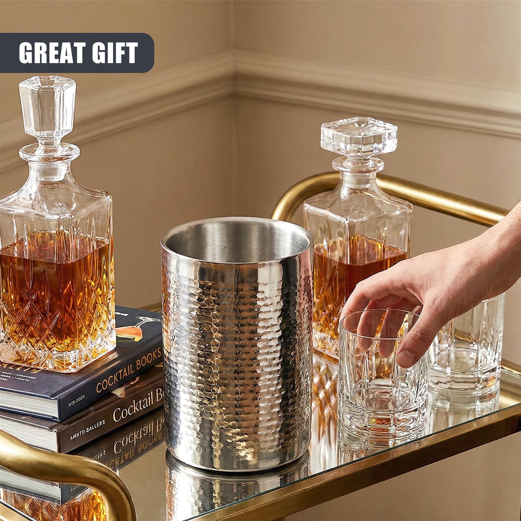 The textured stainless steel wine cooler rests among books, bottles, and tumblers on a metal tray.