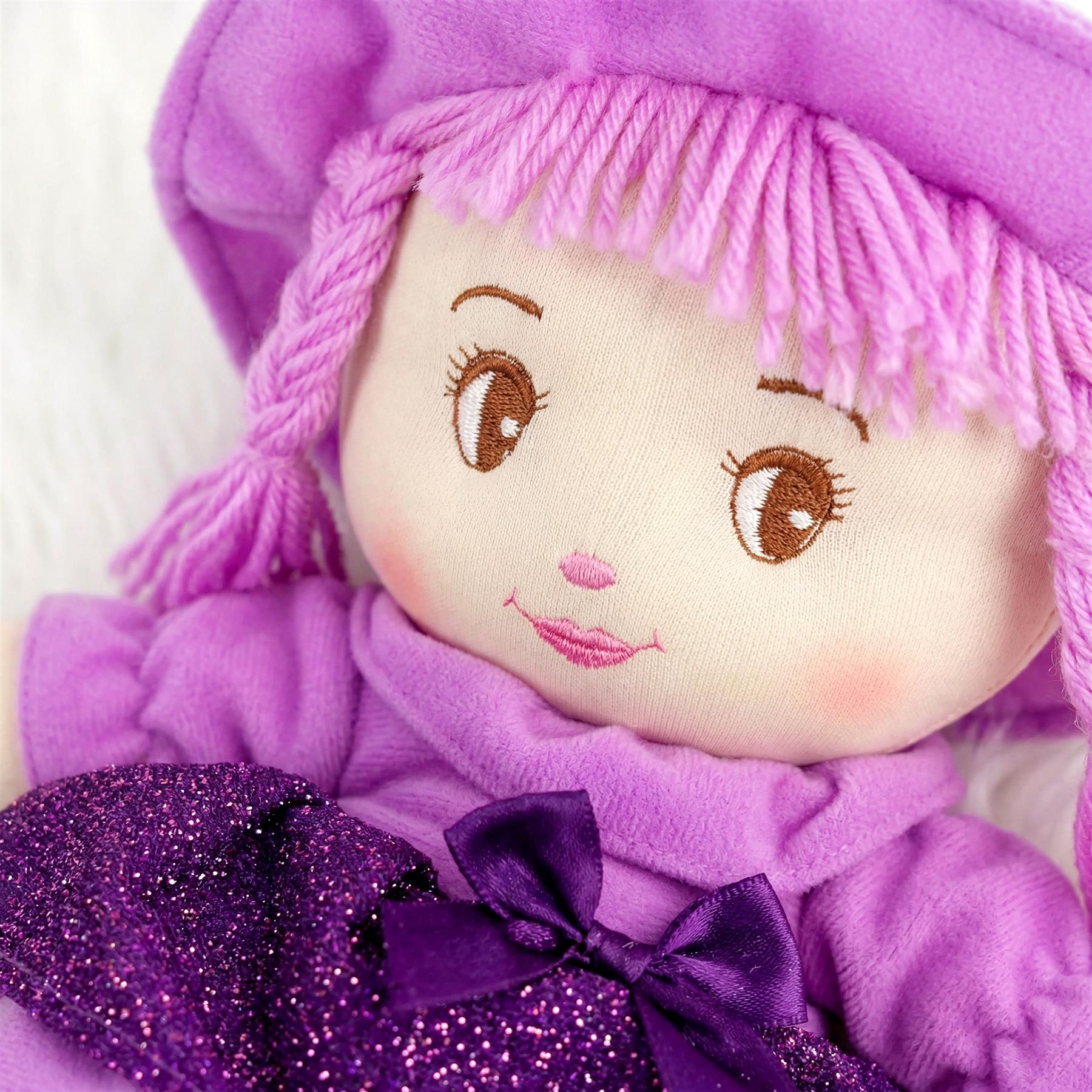 Embroidered rag doll wearing a lavender hood, with visible yarn hair and a shimmering purple bow.