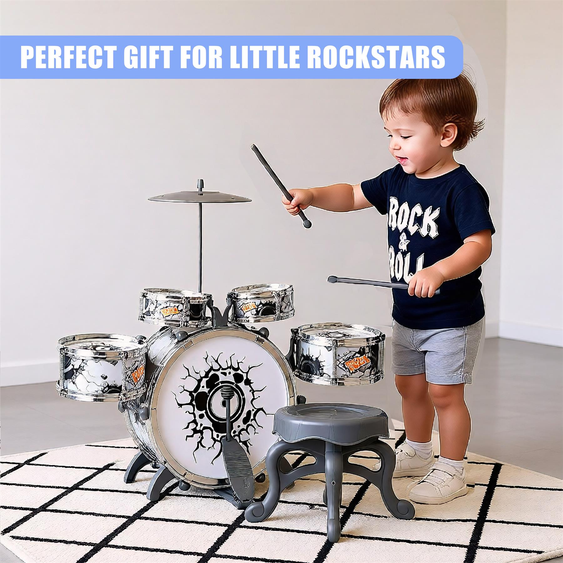 A child stands next to a drum set, holding drumsticks. The drum set has a white and black design with a large drum in the center featuring a black sunburst design. The child wears a black t-shirt with "ROCK" and a small drum on it, gray shorts, and white sneakers. The drum set sits on a white and black rug, with a gray stool in front of it. - The Magic Toy Shop