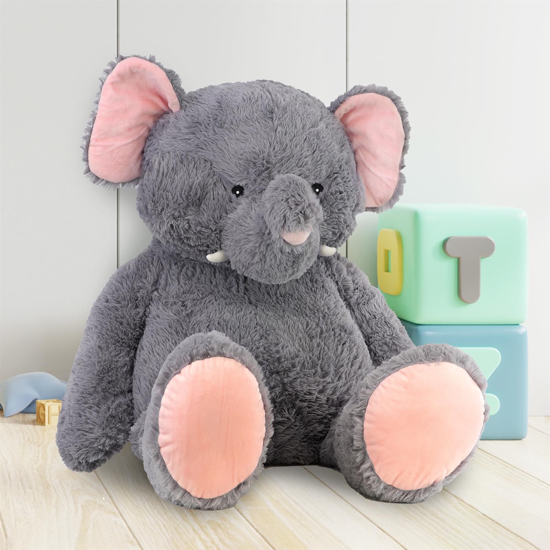 Large plush gray elephant toy sits among stacked colorful educational letter blocks on a wood floor.
