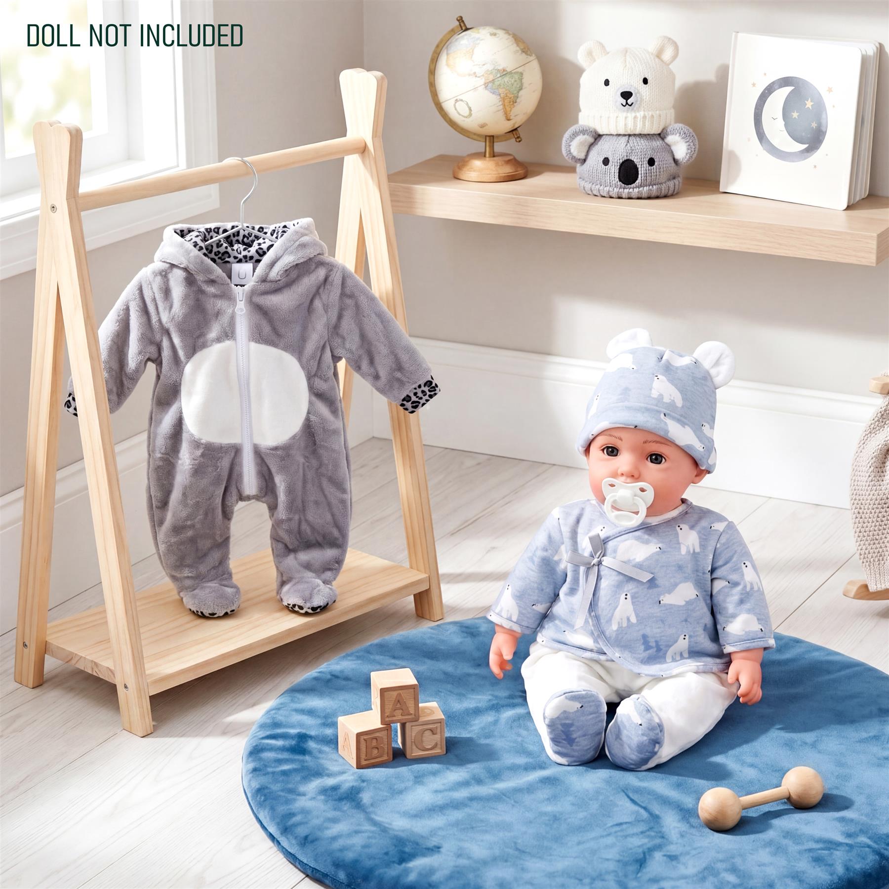 Plush doll wearing blue clothes sits on a mat next to hanging gray and patterned animal outfits.