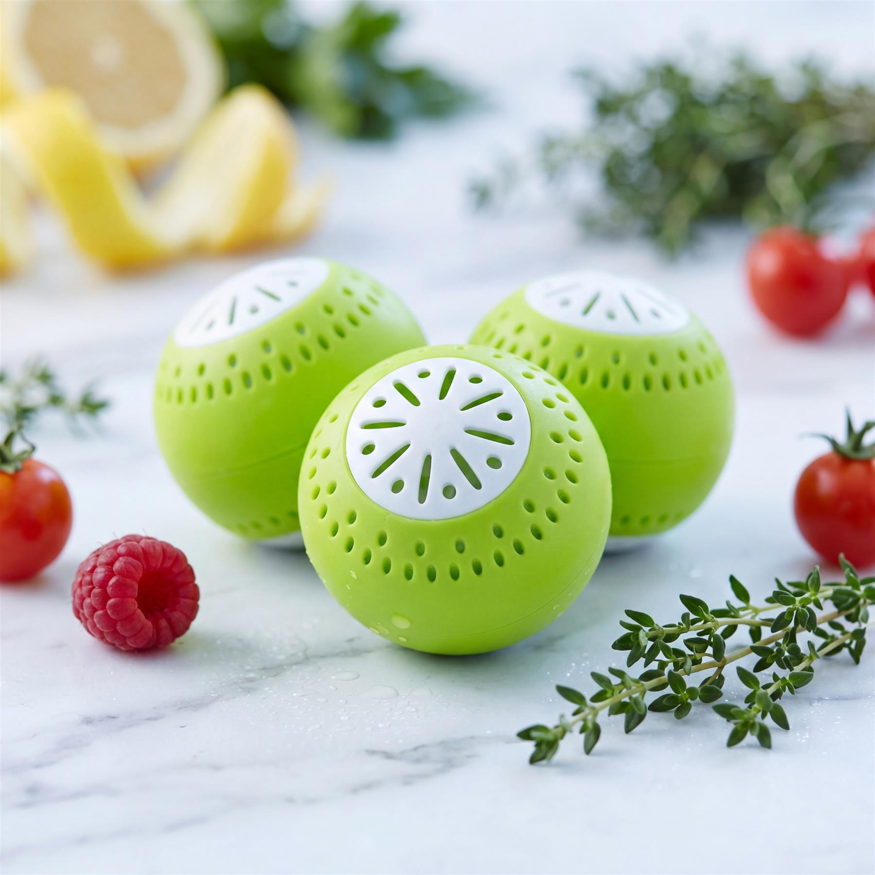 Set of three bright green balls with white decorative cutouts, displayed with fresh fruit and herbs.