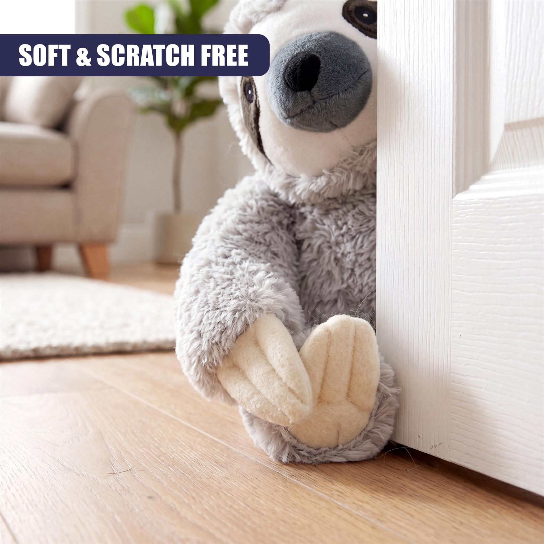 Plush grey sloth character wedged against a white door frame on hardwood flooring.
