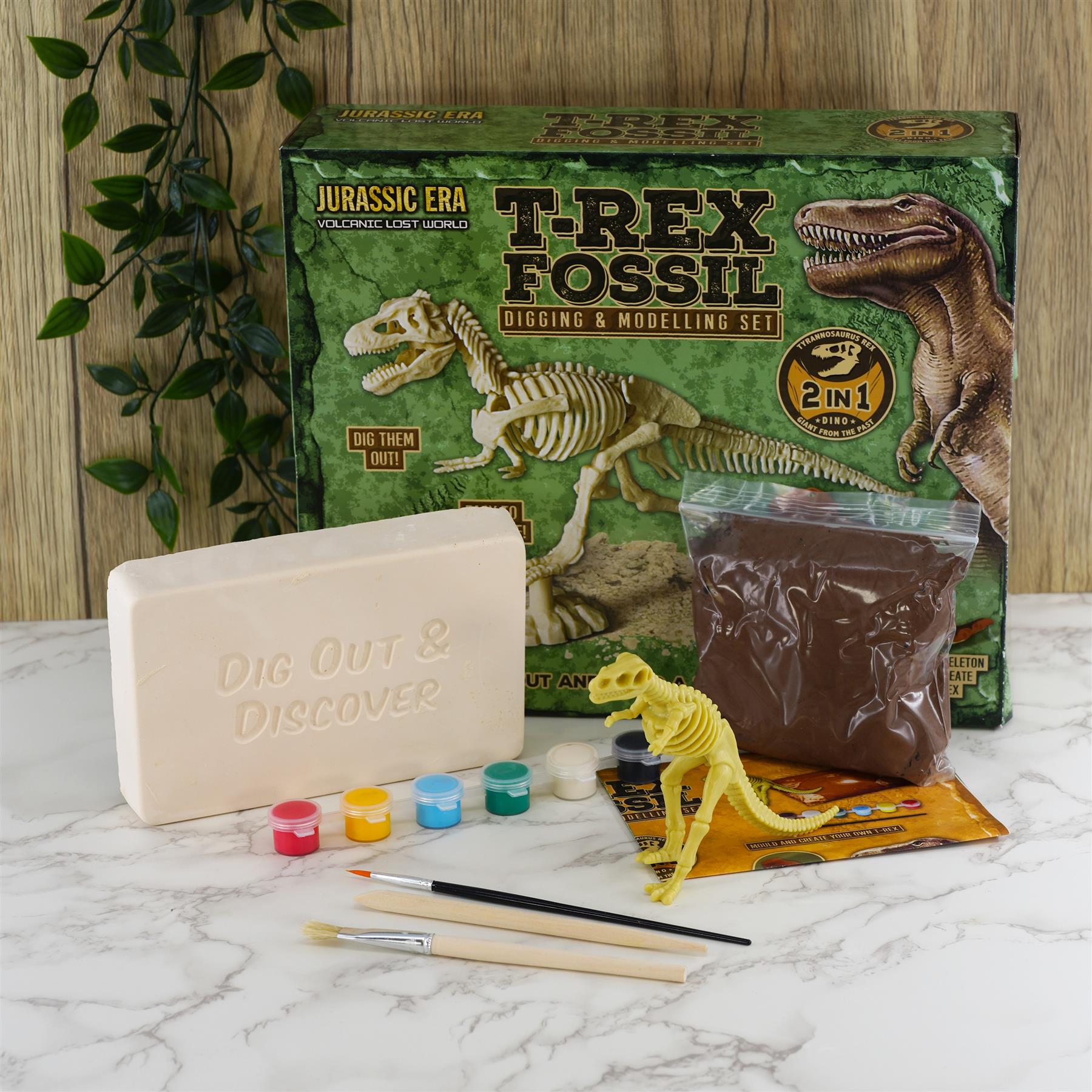 A fossil kit showing light beige clay, dark clay, plastic skeleton, small caps, and paintbrushes.