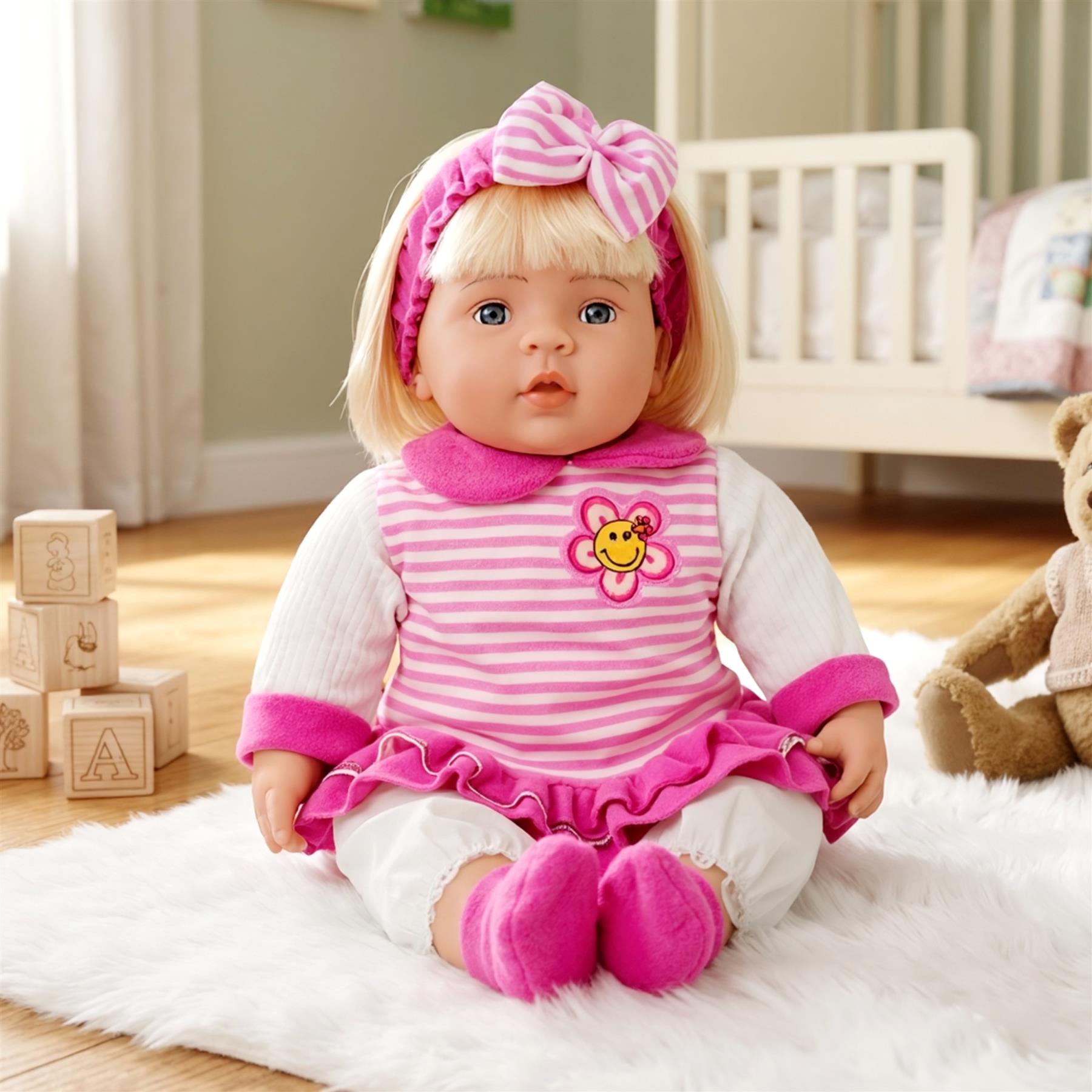 A large doll of a chubby baby girl wearing a fitted pink dress, bonnet, and headband.