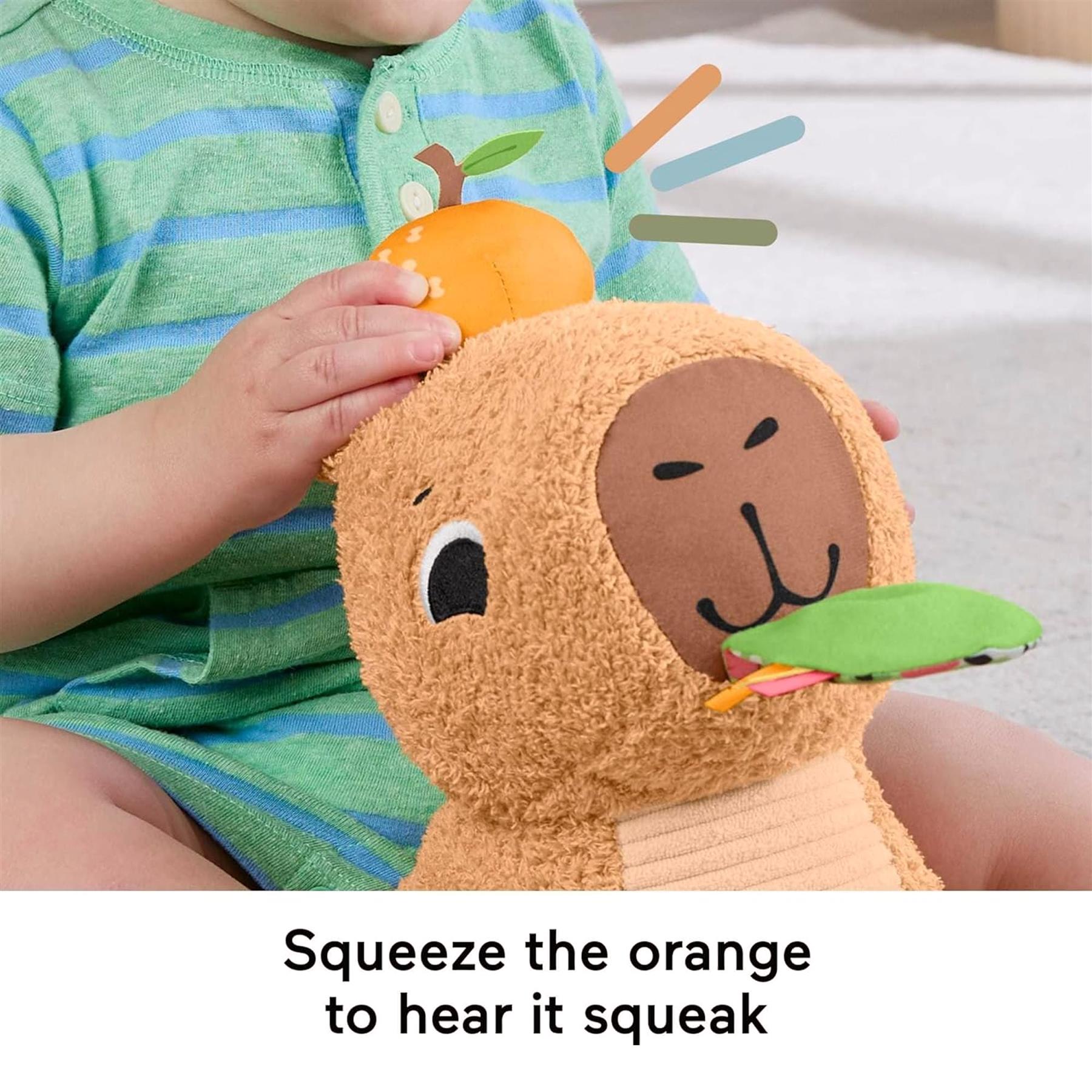 Child's hand presses an orange ball on a plush capybara holding a green snack.