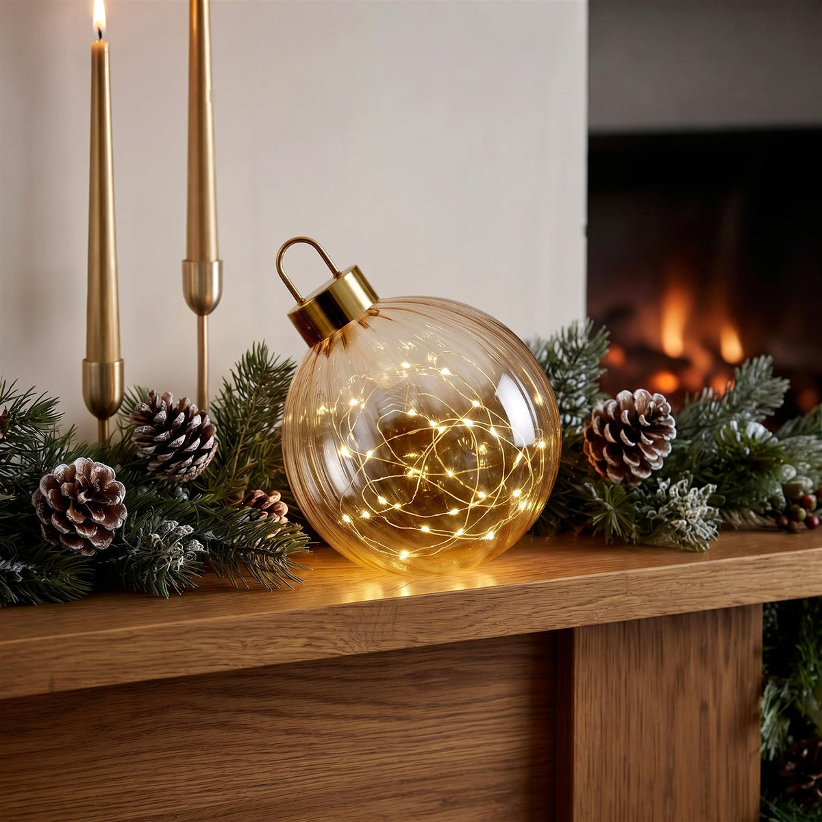 Light Up Amber Glass Bauble ornament with warm white LEDs sits on a wooden mantelpiece