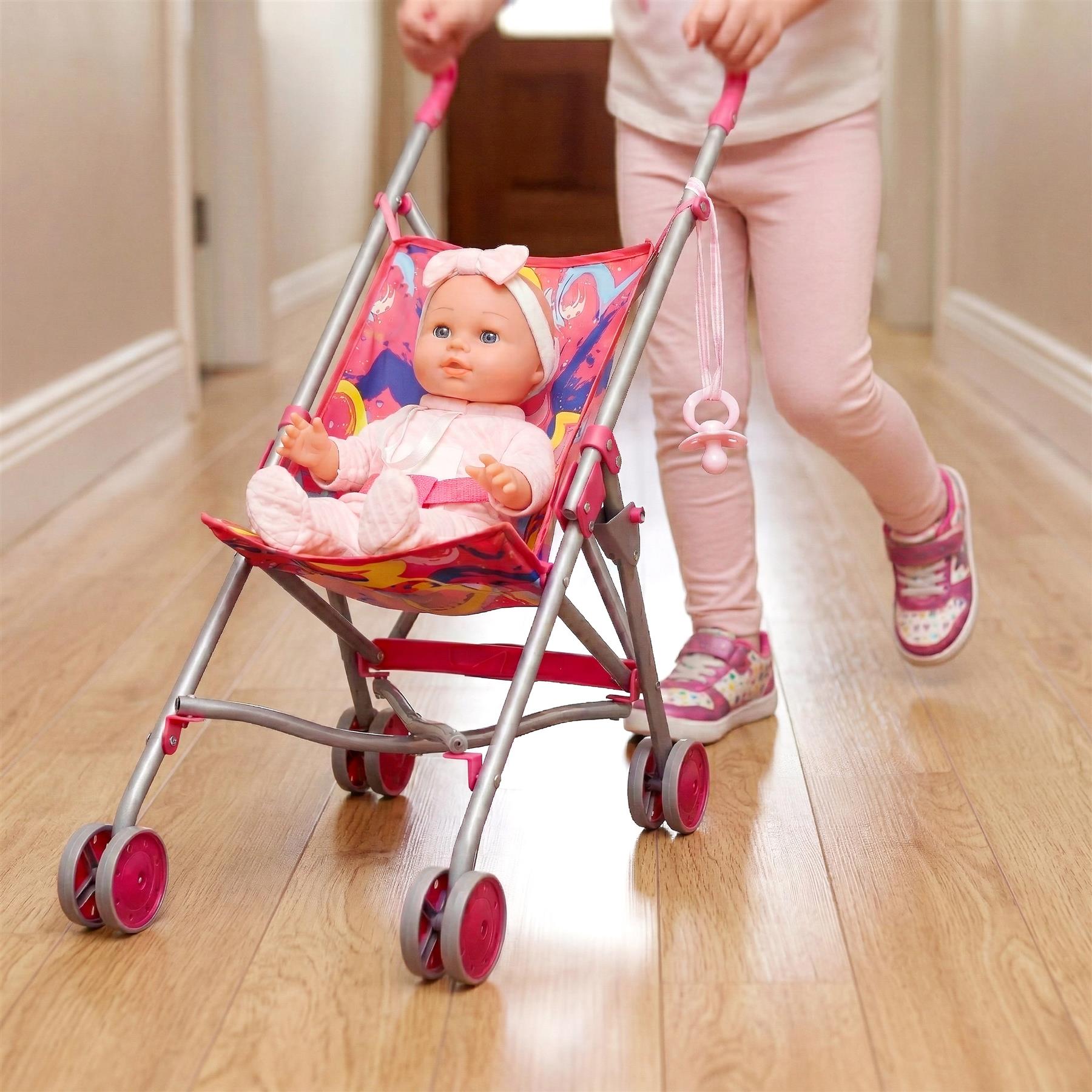 Pink baby stroller with four wheels, containing a doll, being pushed down a wooden hallway.