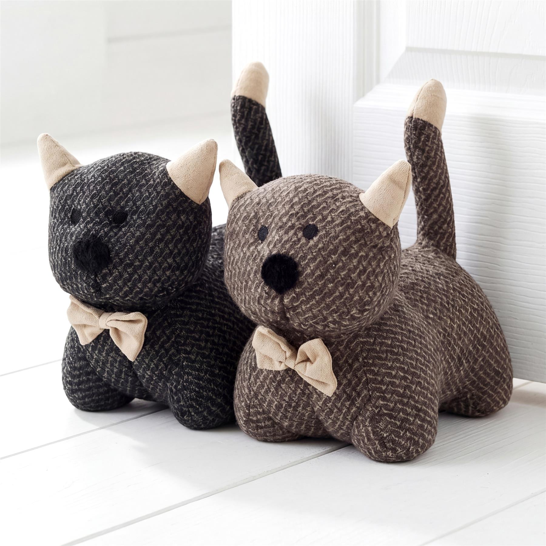 Three fuzzy, striped stuffed bears wearing bows sit together on a light wooden surface.