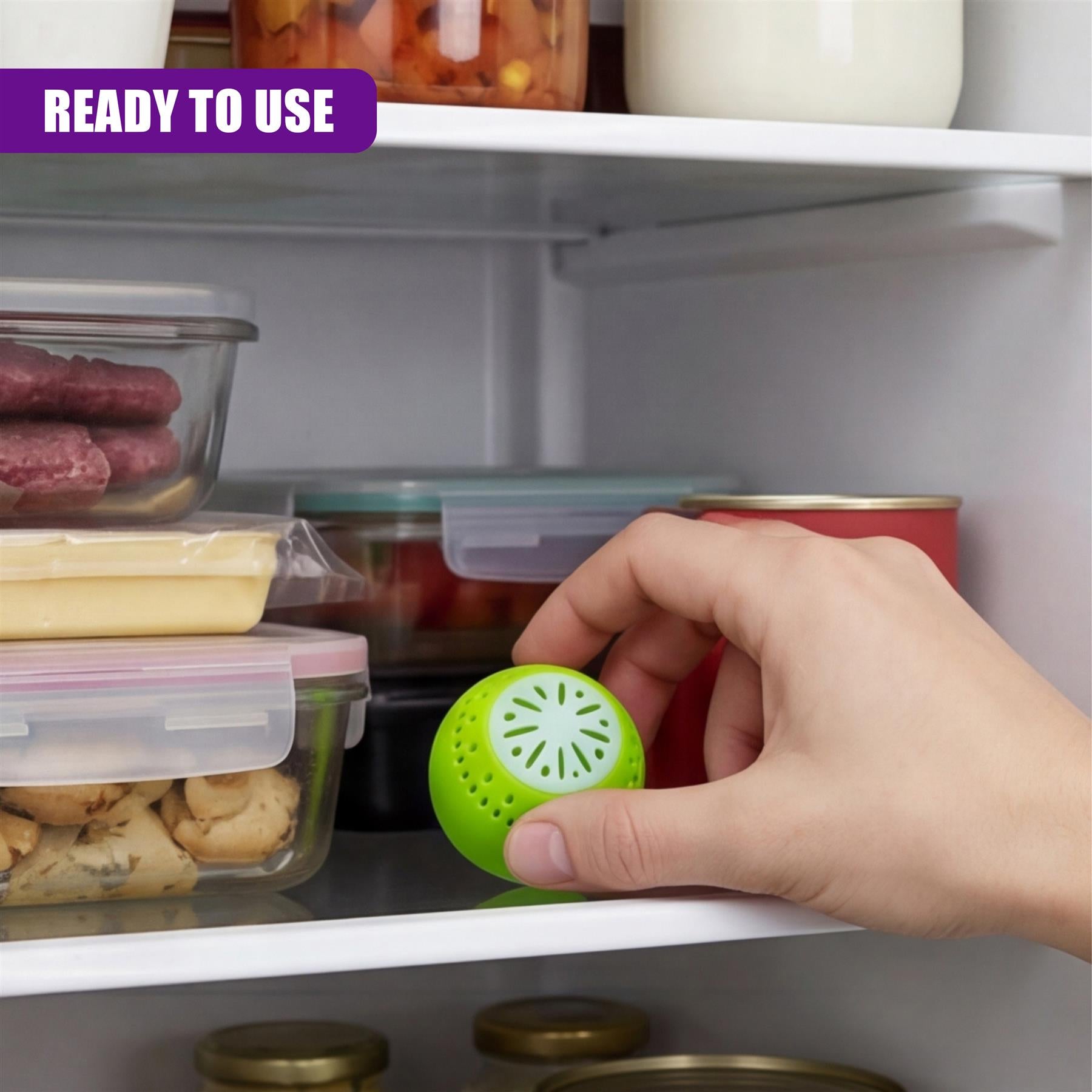 A hand places a bright green, porous deodorizer ball inside an open refrigerator shelf.