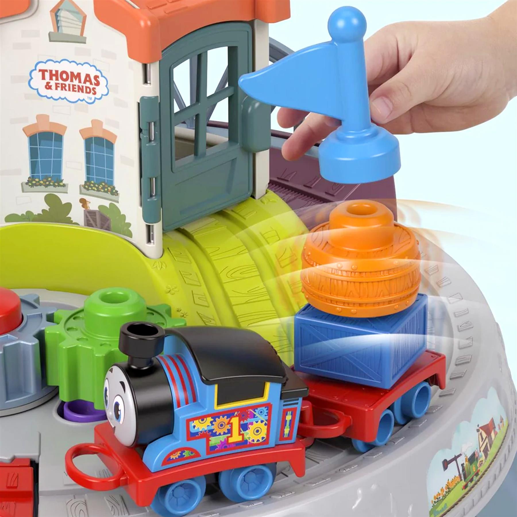 A hand places a blue piece onto the tracks alongside a Thomas train and colorful stackable car set.
