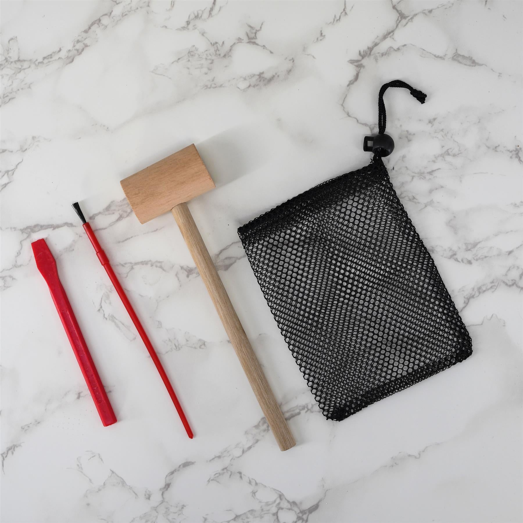 Wooden handled pick, two red digging tools, and a small black mesh bag rest on white marble.