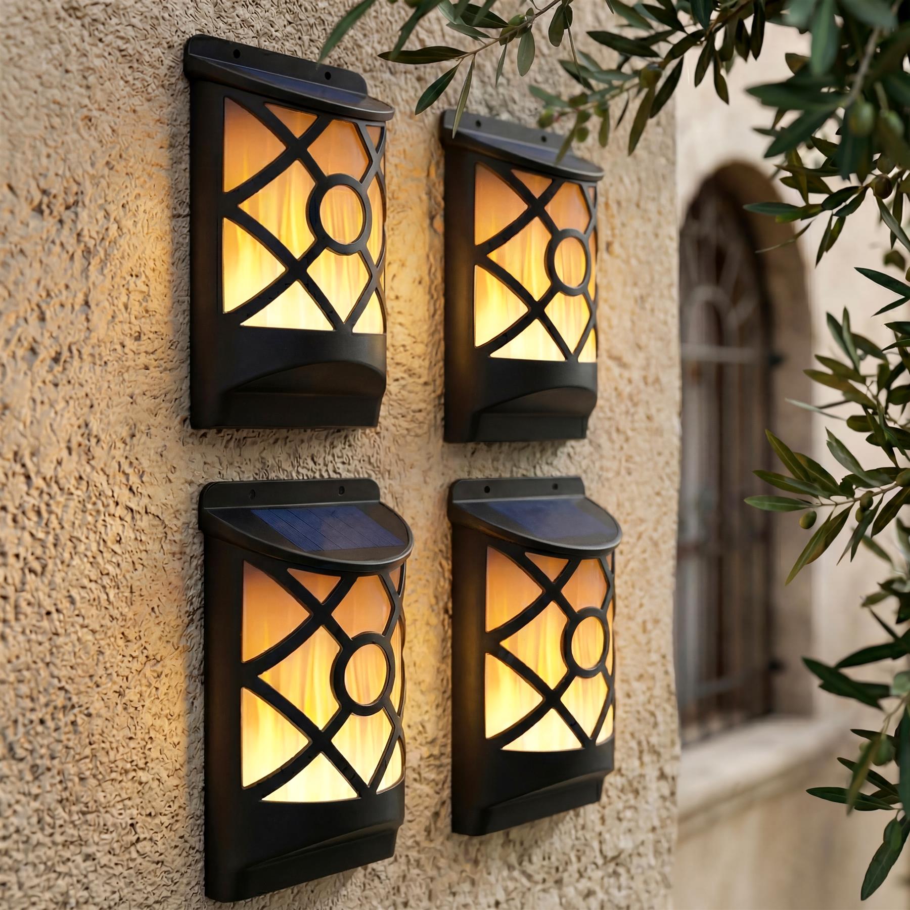 Four patterned wall lanterns cast warm light on a textured stone wall with visible greenery.