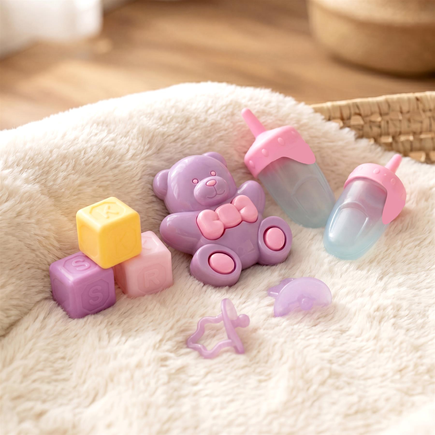 Purple bear figure, letter blocks, and baby accessories rest on a fluffy cream-colored fabric.
