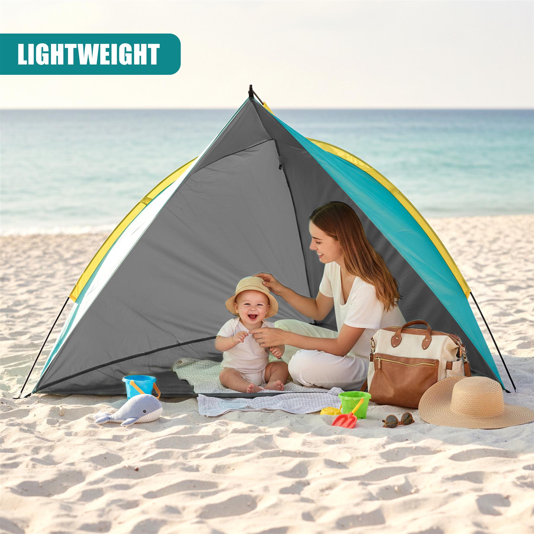 A woman and baby sit outside a pop-up beach tent on the sand by the ocean.