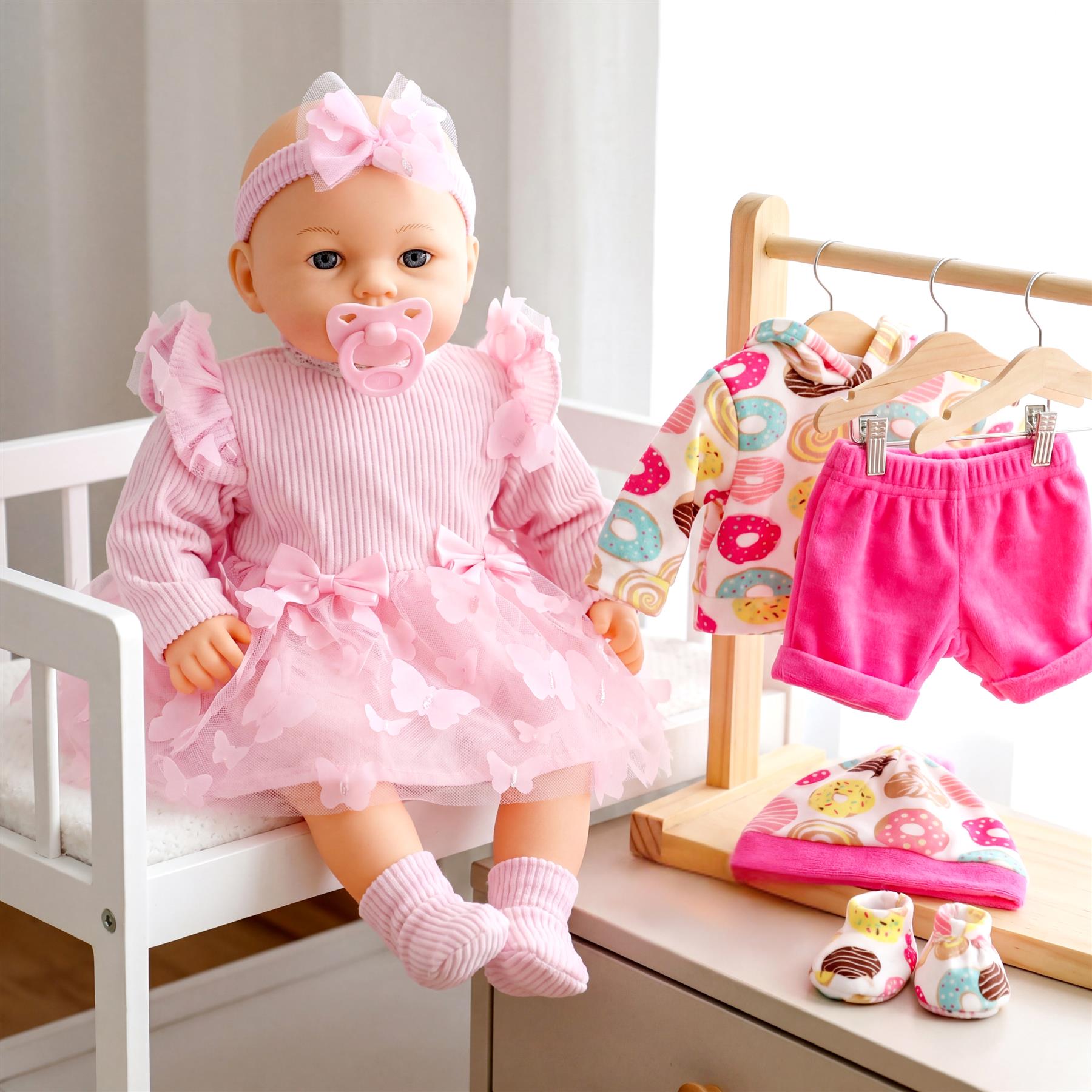 Doll in pink outfit sits near various matching clothing accessories, patterned top, and shorts.