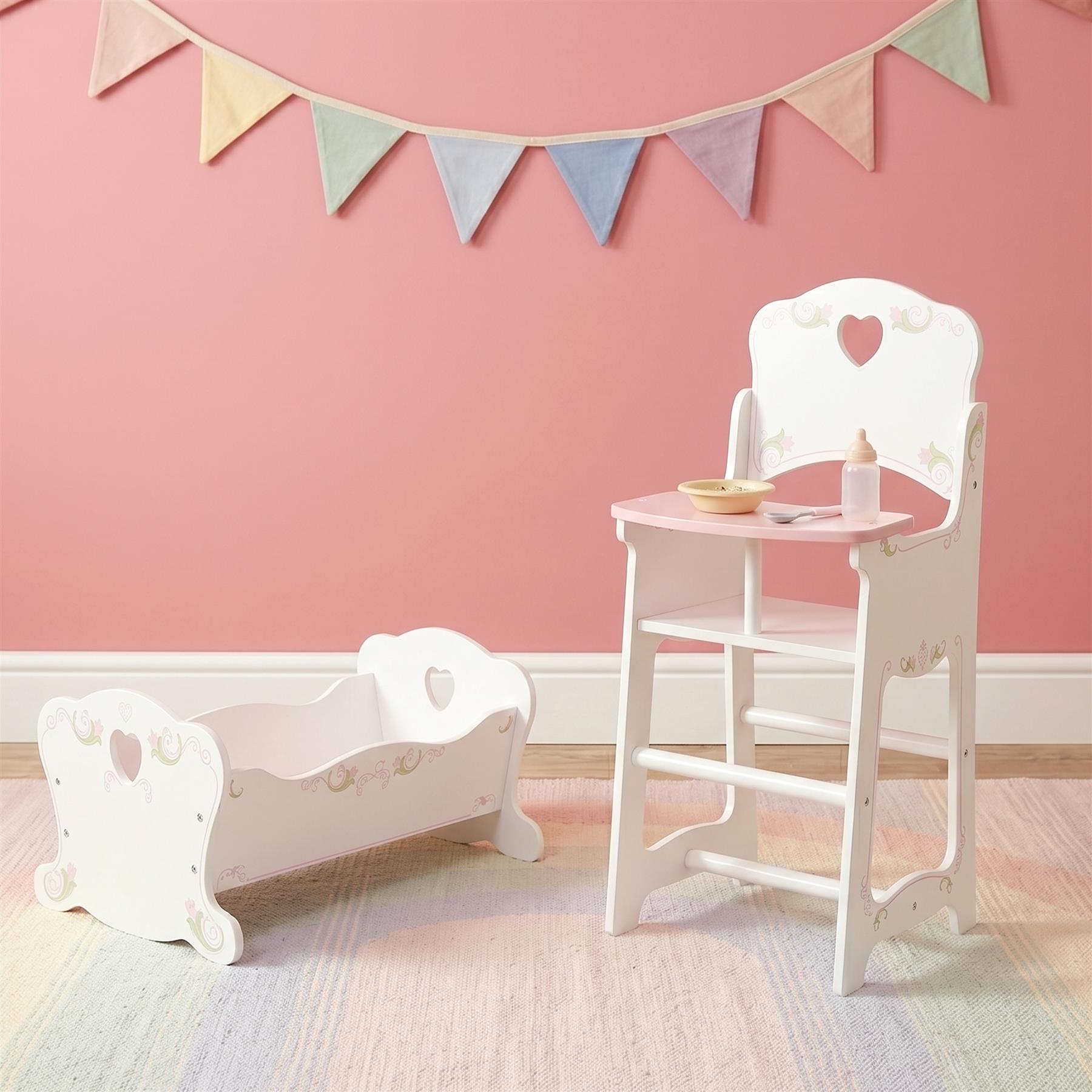 White wooden doll cradle positioned next to a matching white wooden high chair and table set.