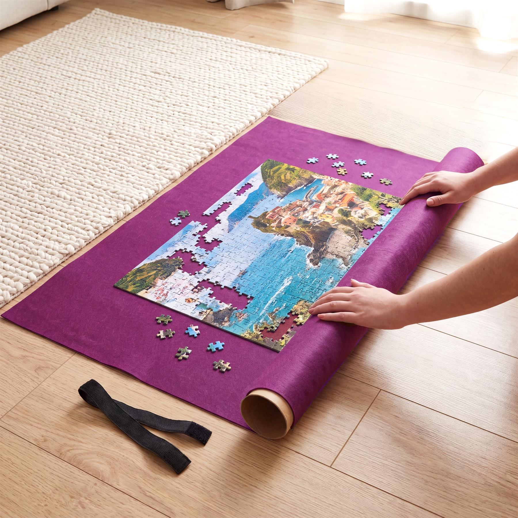 Hands are placing a photo jigsaw puzzle on a purple rolling mat on a light wood floor.