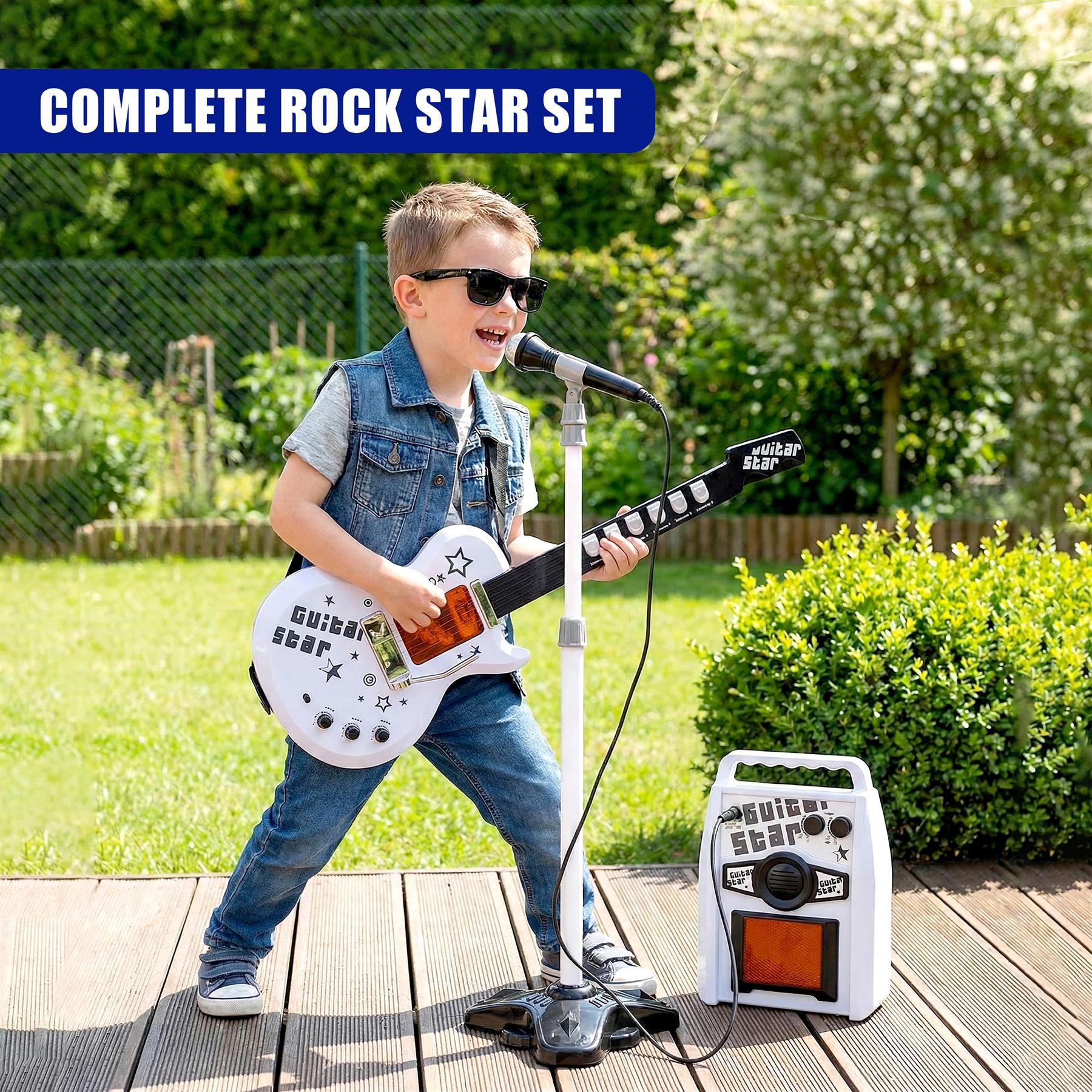 Outdoors, a boy holds a white guitar with microphone and small amplifier set.
