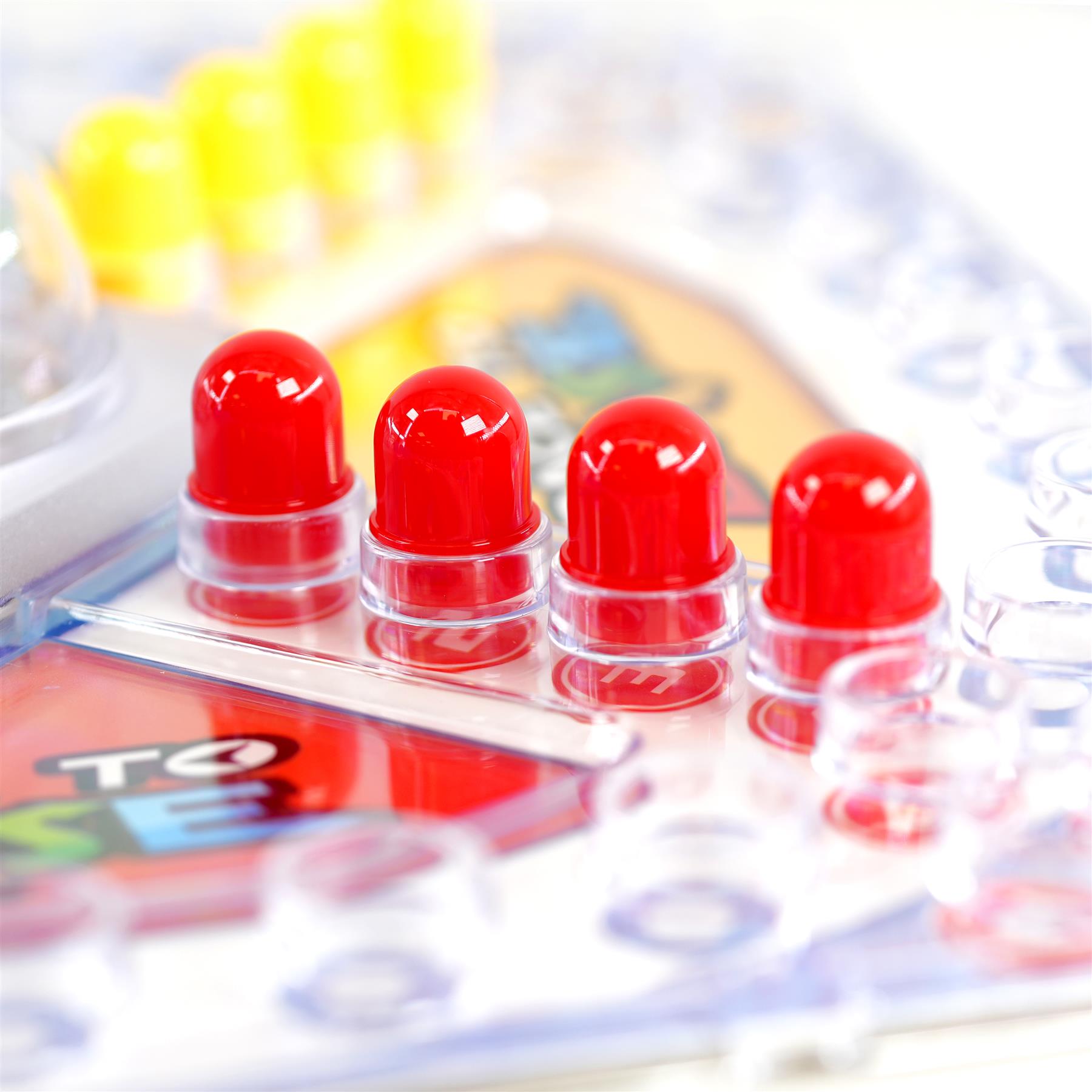 Four red plastic game pawns are displayed on a race board next to yellow tokens.