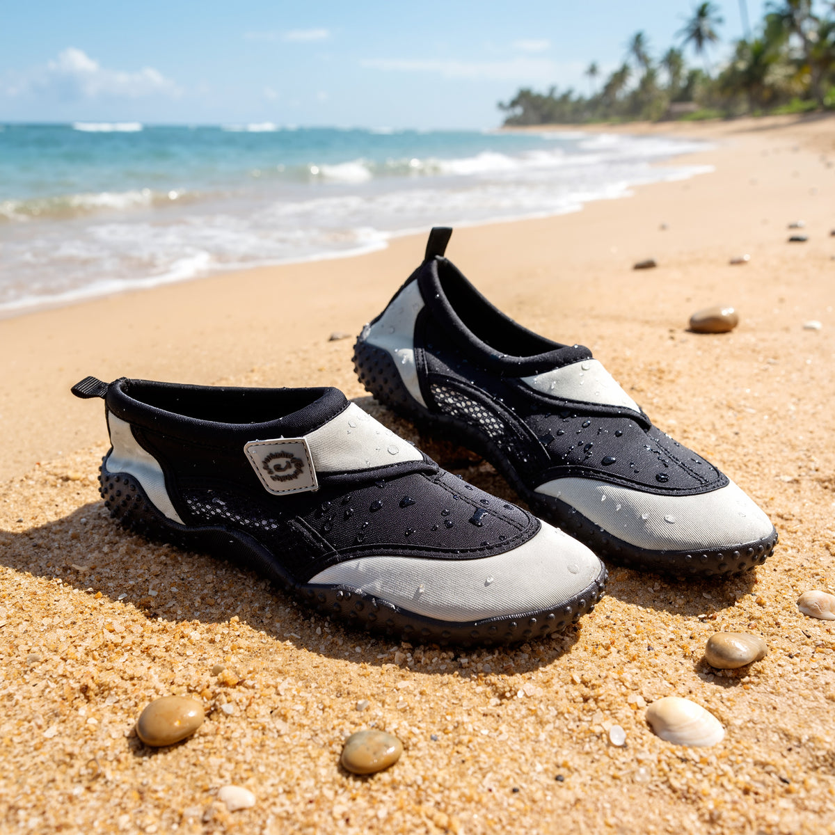 Grey GEEZY aqua shoes sit on sand beside the sea, ready for water adventures